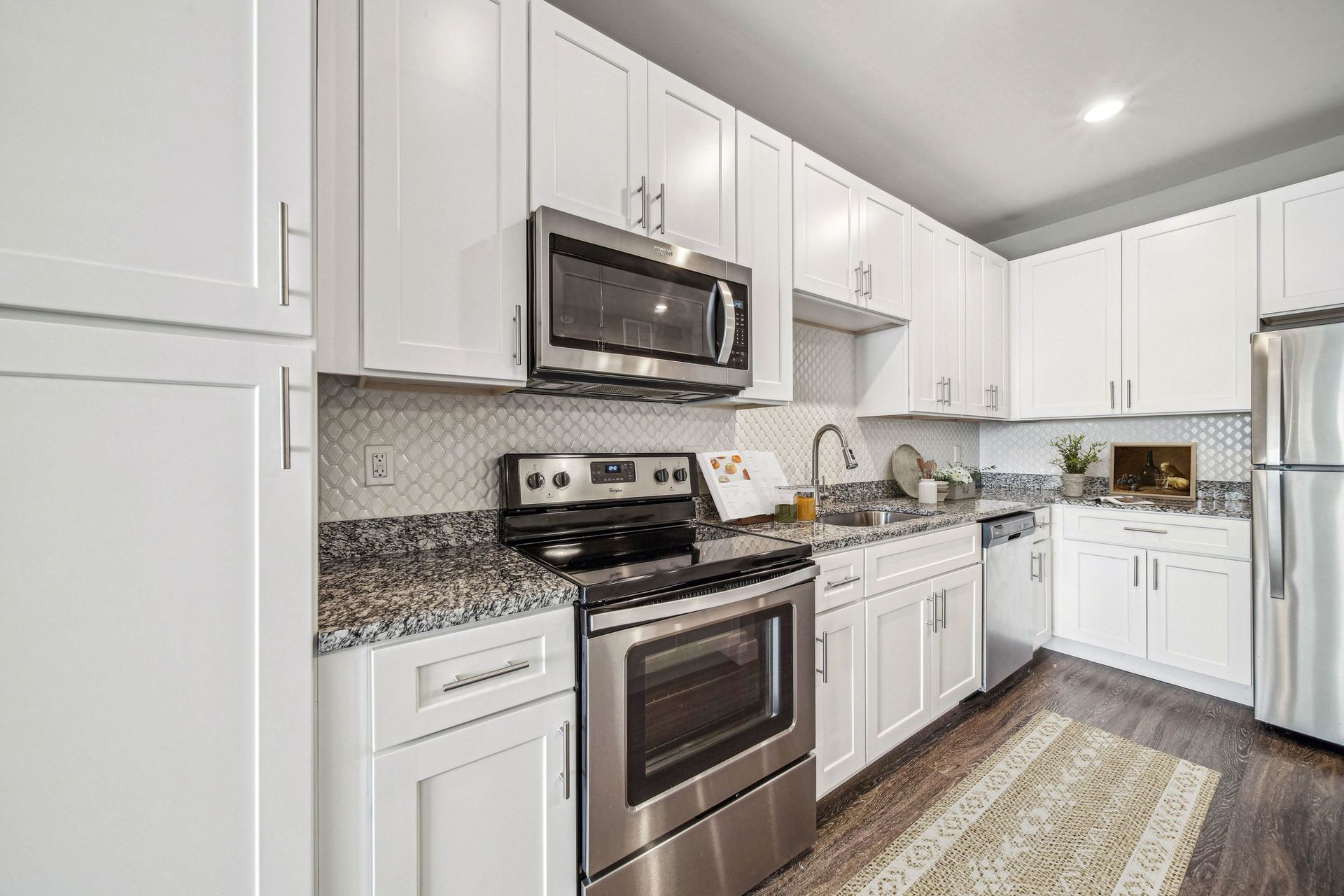 Modern white kitchen with granite countertops, stainless steel appliances, and a double sink.