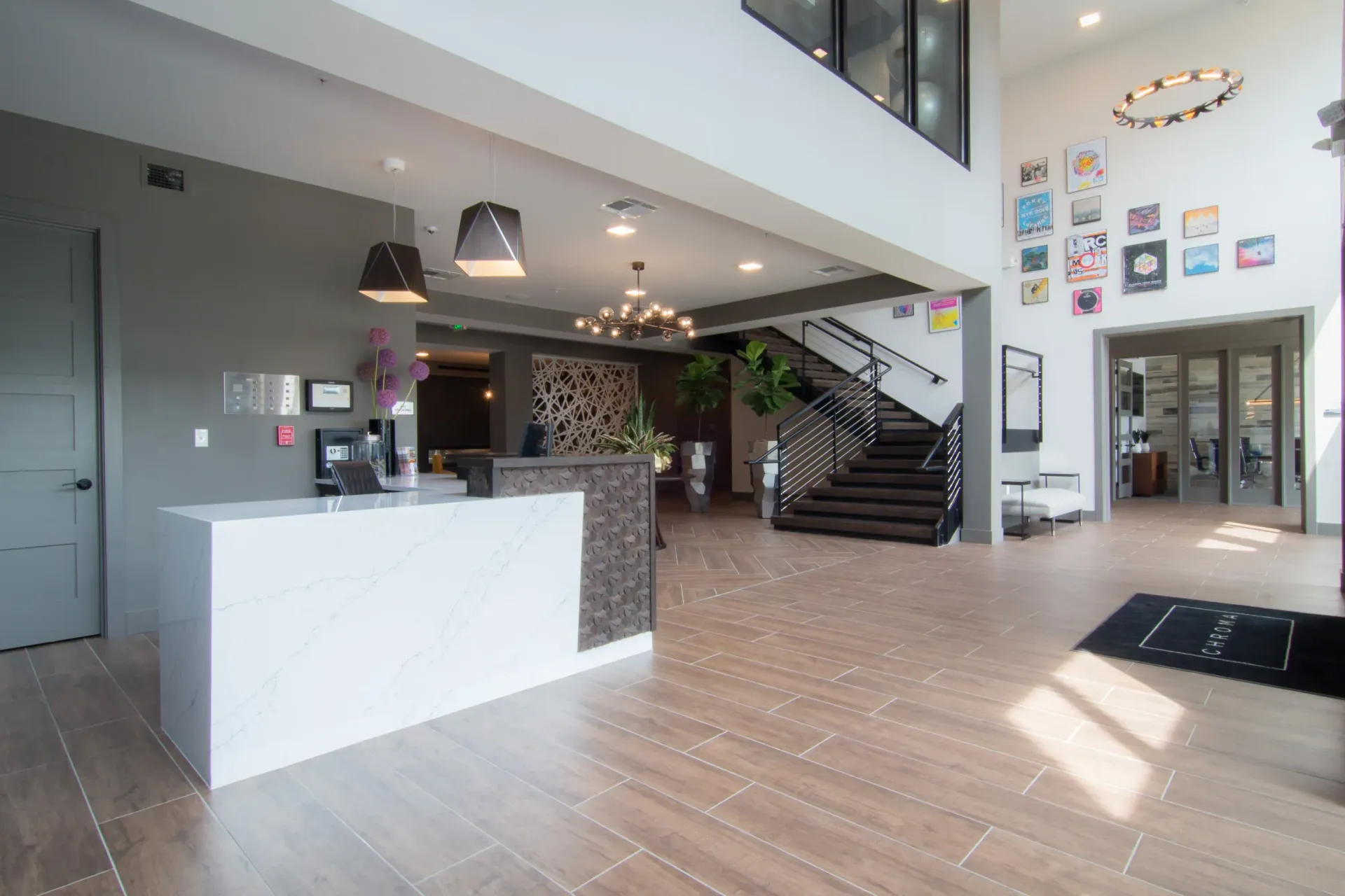 Modern apartment lobby with a white marble-front reception desk, staircase, and wall art.