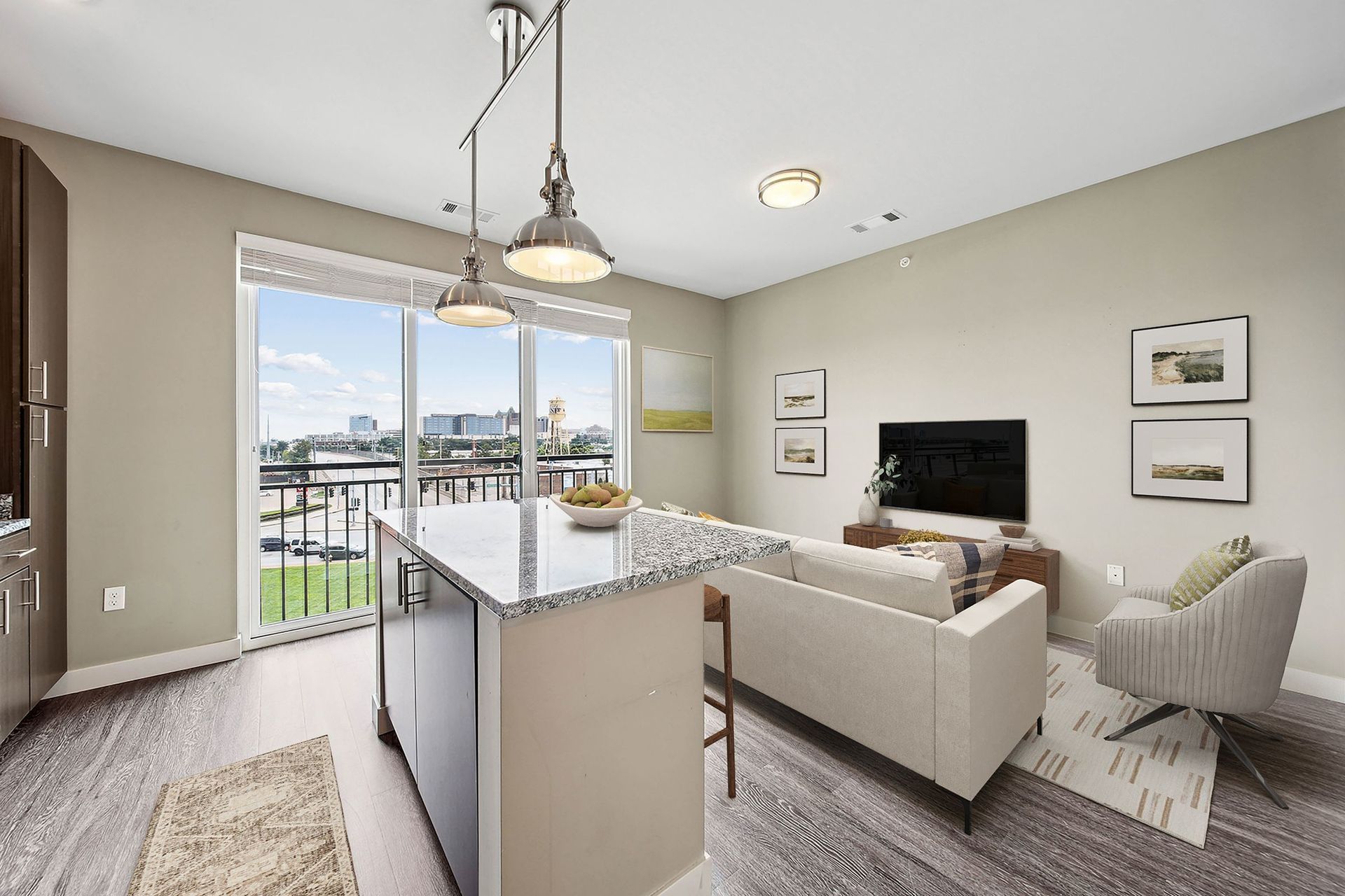 Open-concept living area in a modern apartment with a granite island, sofa, and large balcony windows.