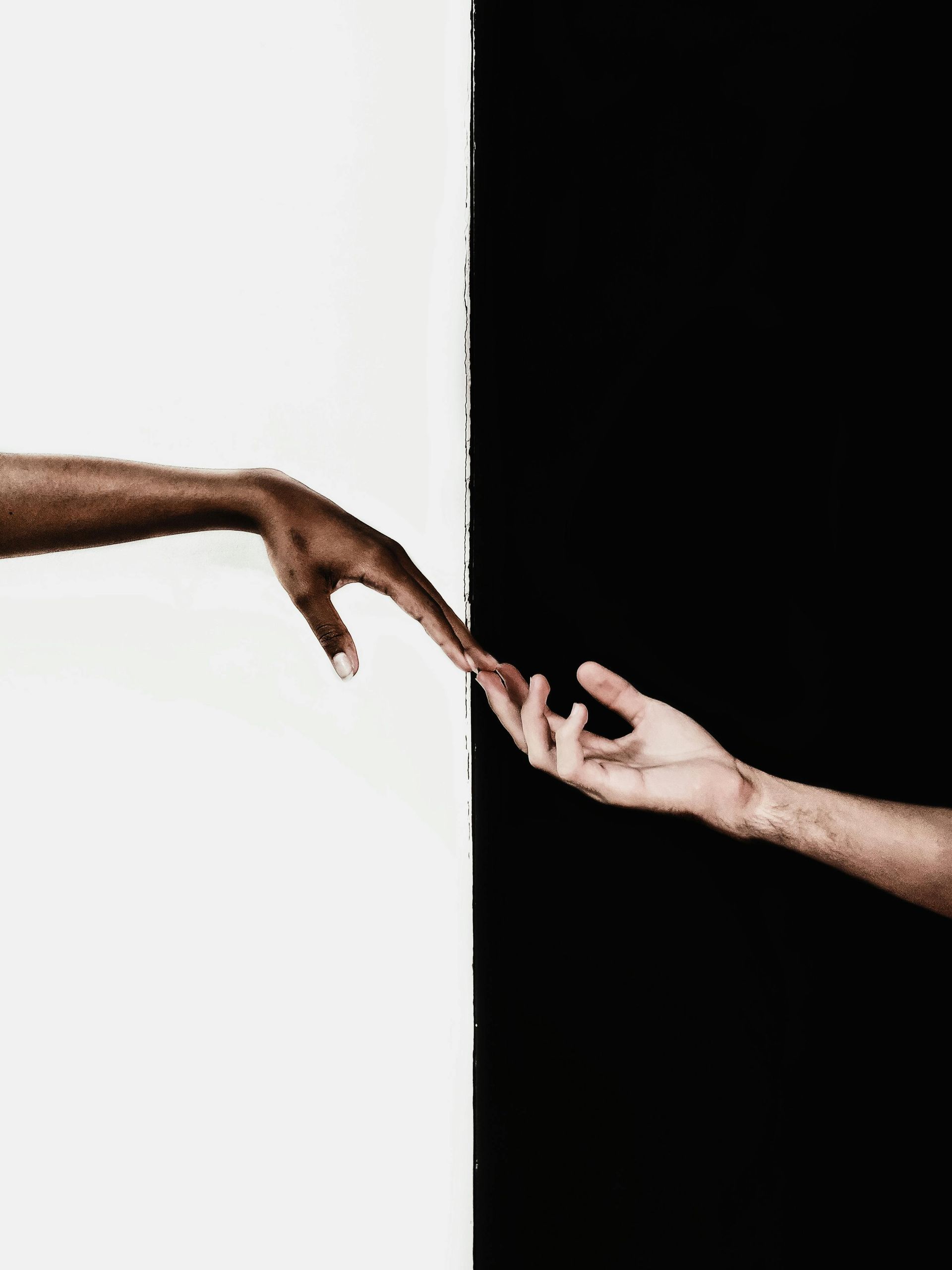 A black and white photo of two hands reaching out towards each other.
