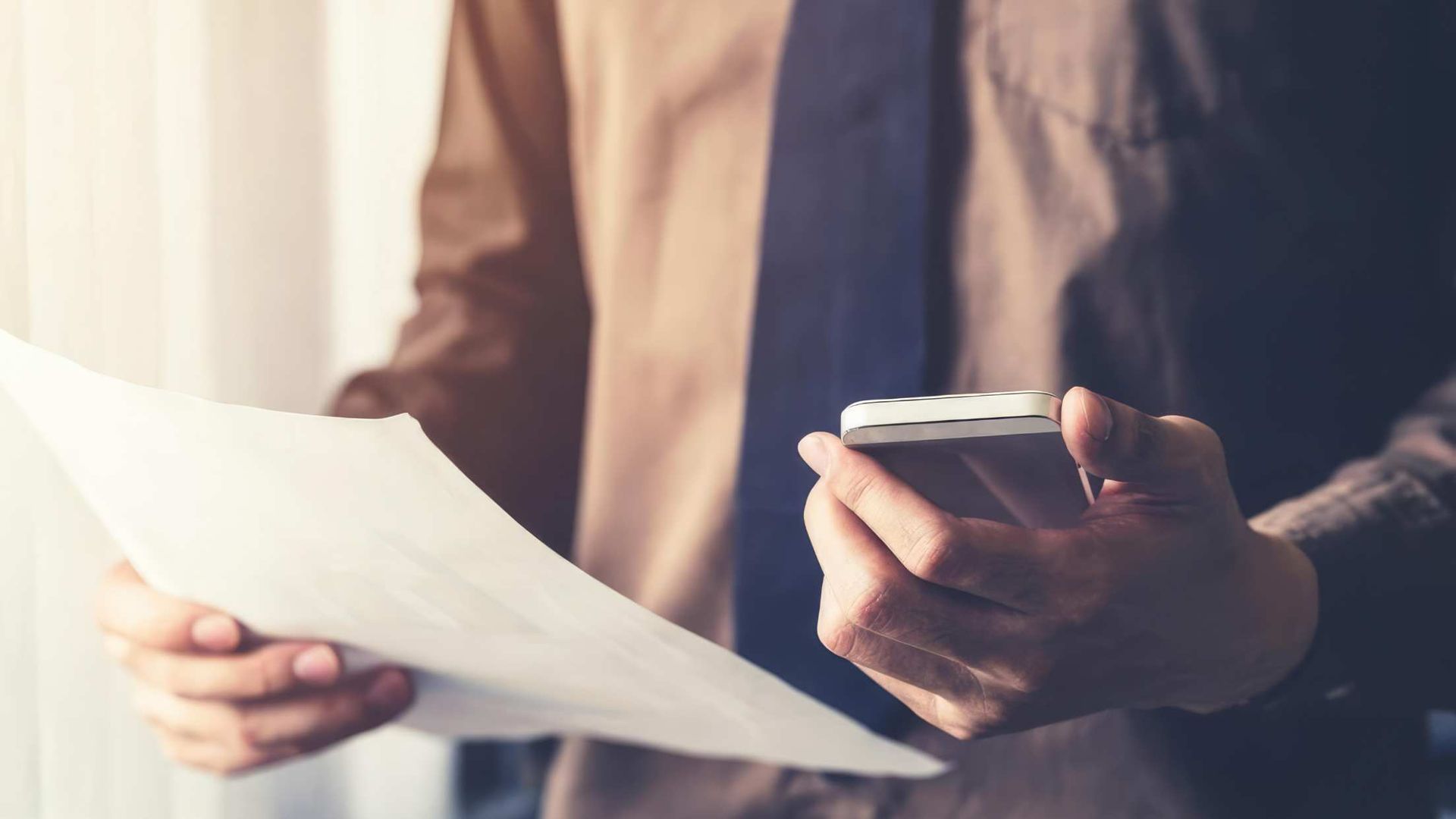 Person holding a paper and a smartphone while reviewing a document indoors