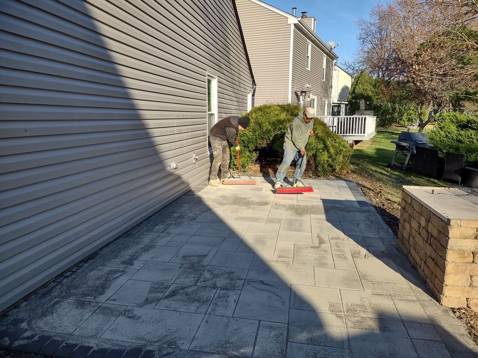Two men are working on a patio in front of a house.