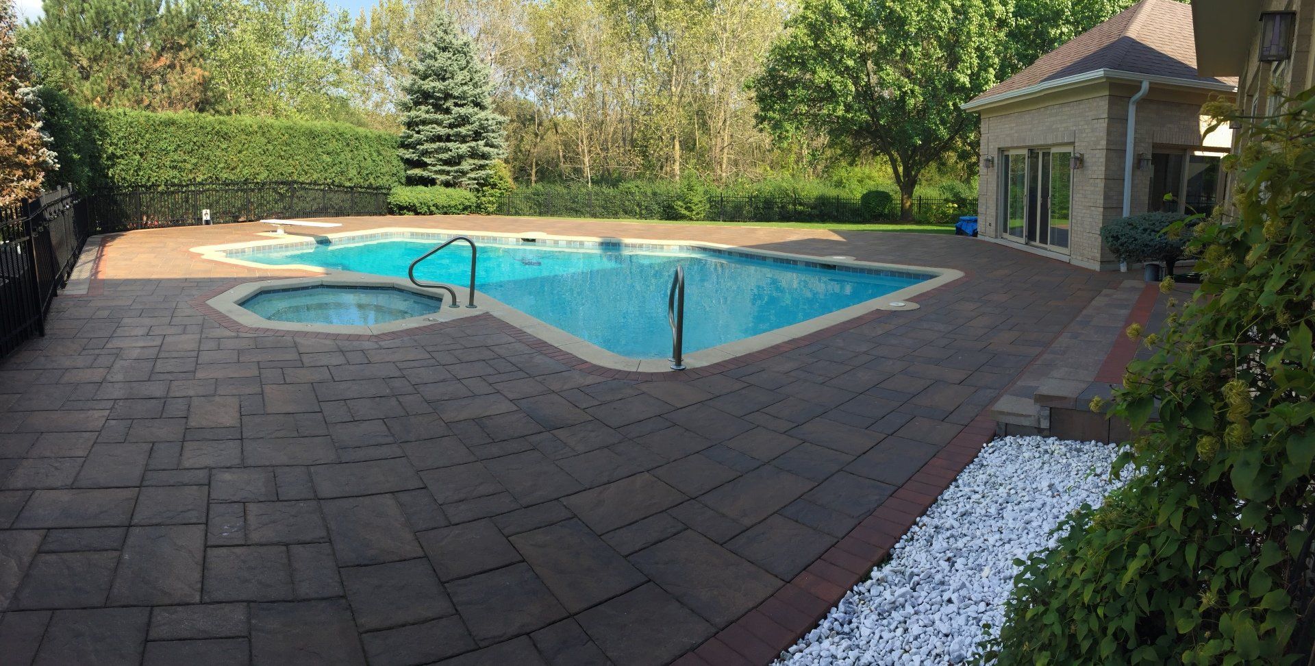 A large swimming pool with a hot tub in the backyard of a house.