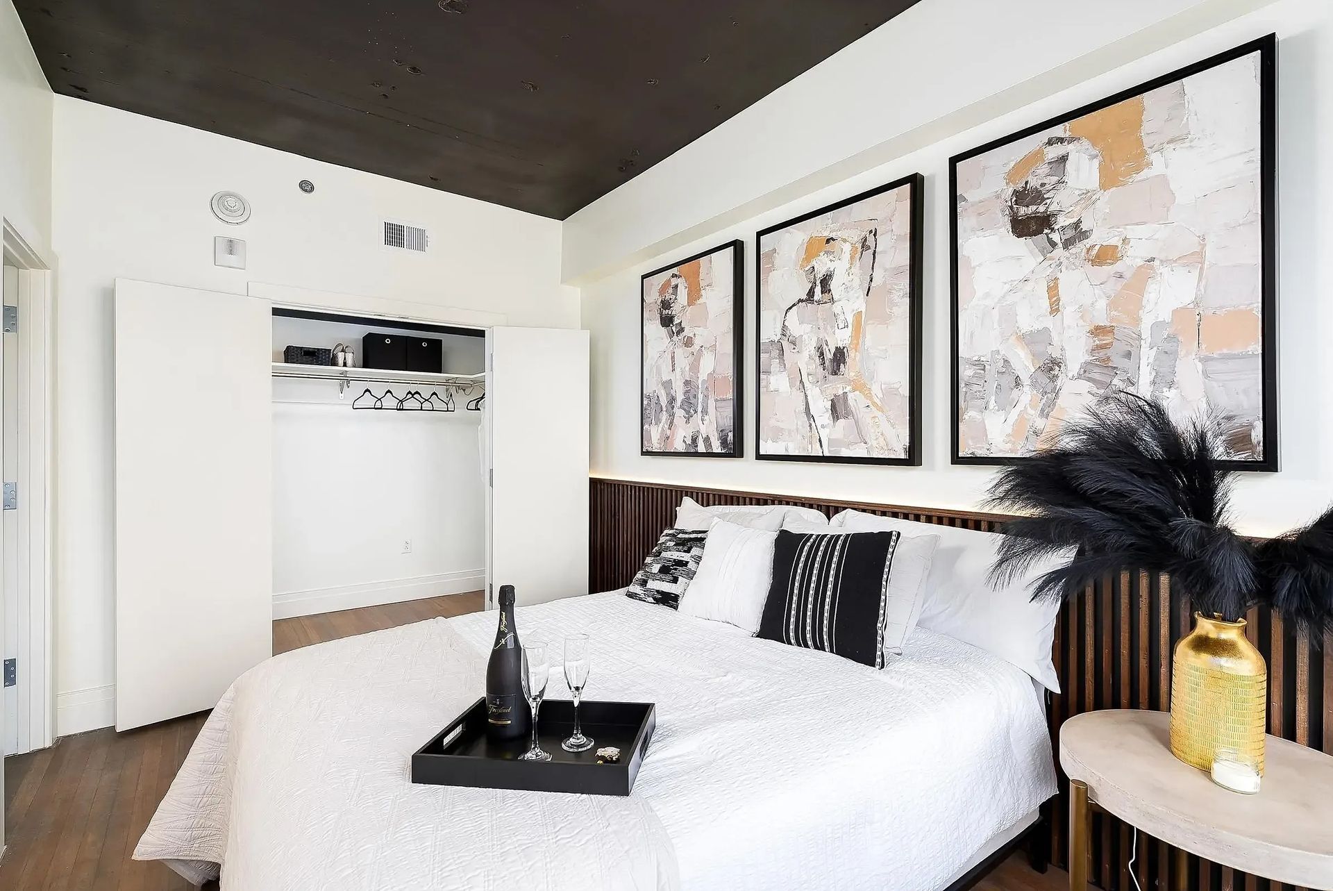Bedroom with white bed, abstract art, black accents, open closet, and a tray of drinks.