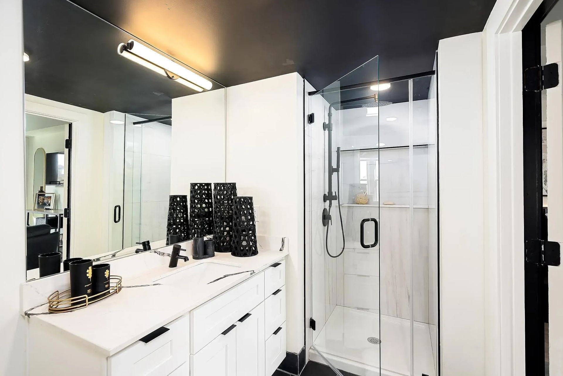 Modern black and white bathroom with glass shower, white vanity, and black accents.