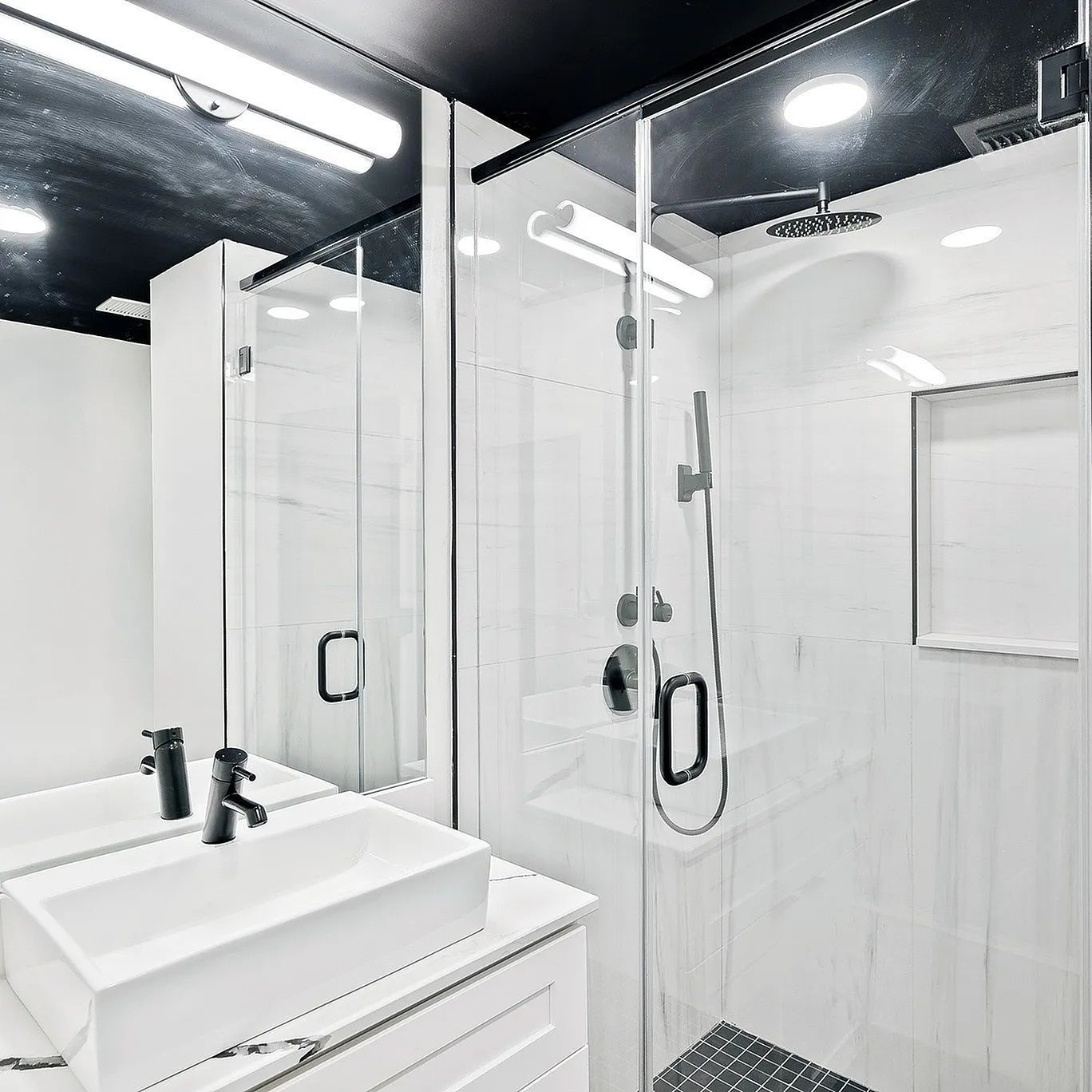 Modern white bathroom with a shower, sink, and black fixtures.