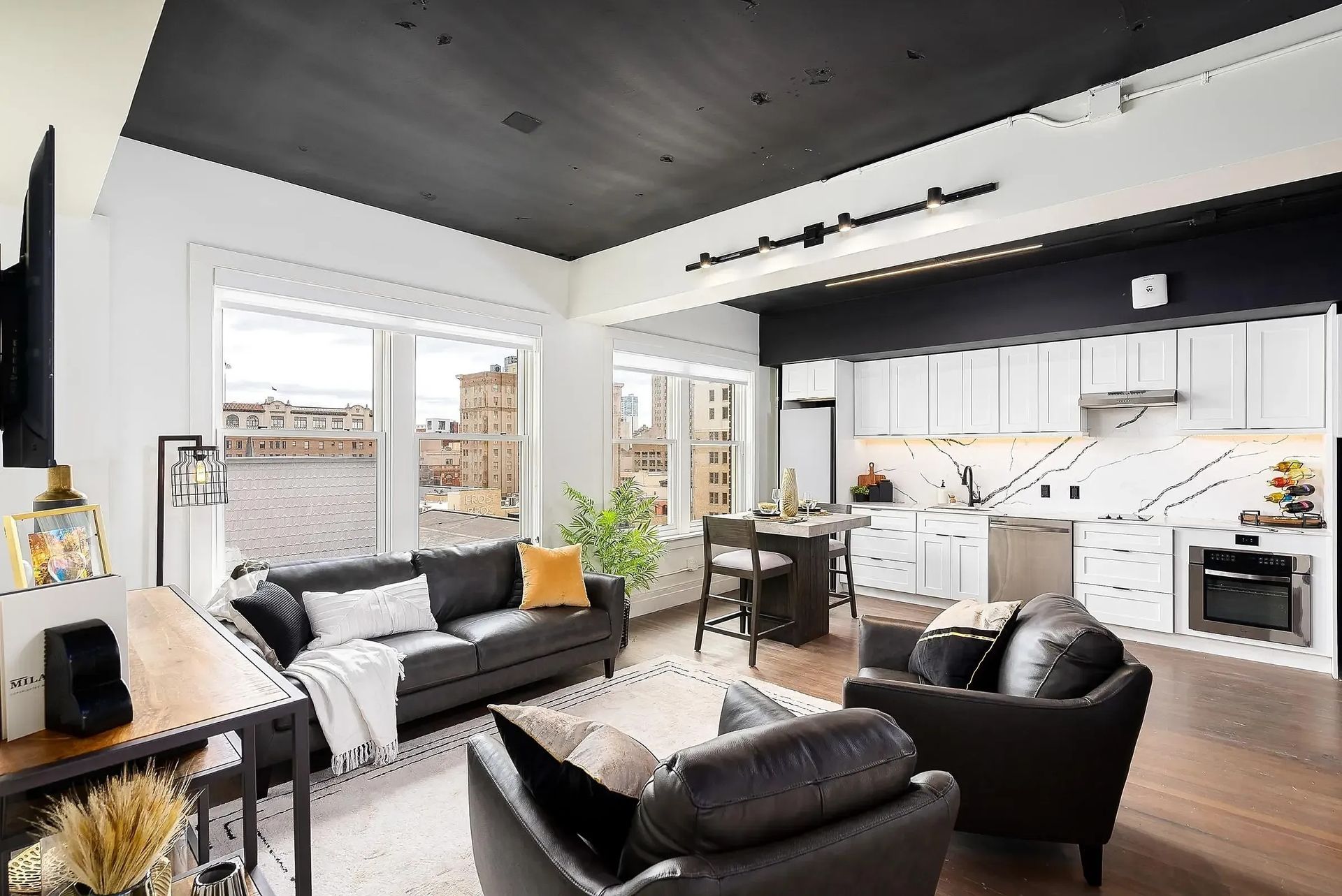 Modern open-concept living space with black and white accents, a kitchen, and large windows overlooking a city view.