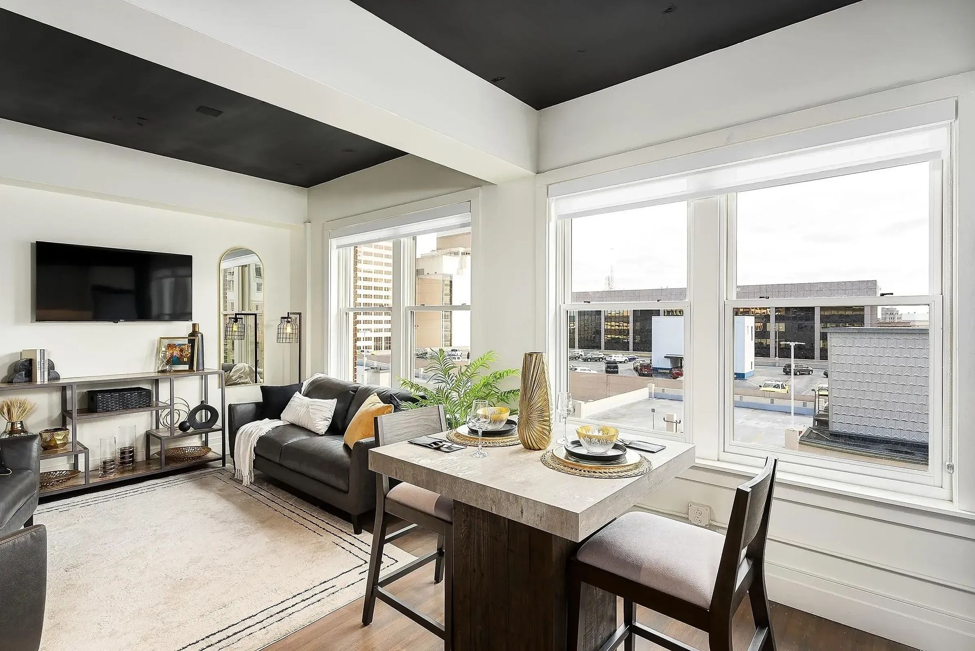 Living area with black ceiling, white walls, dark furniture, and a small dining table by the window.