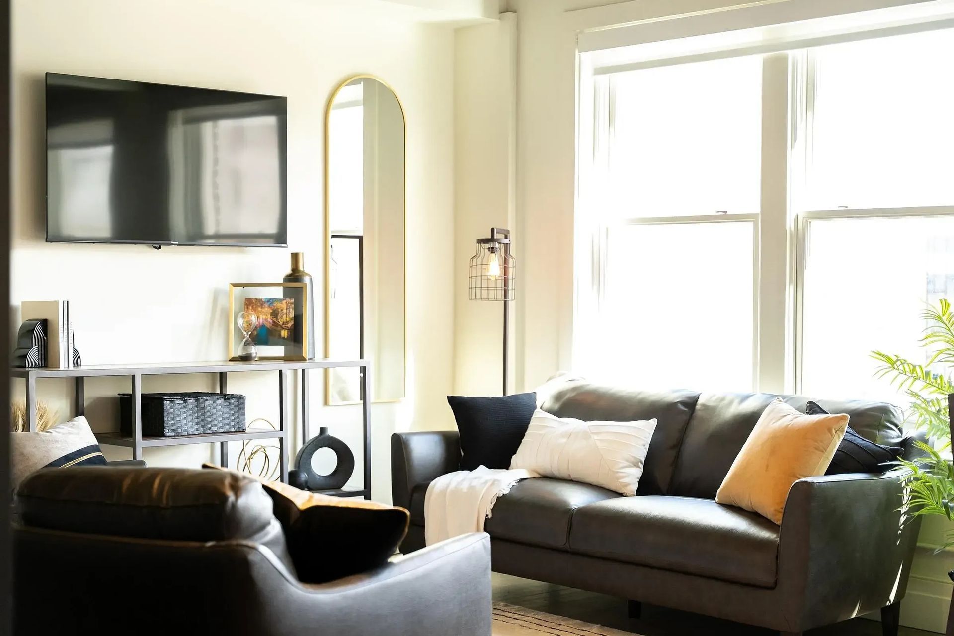 Living room with gray sofa, TV, mirror, and window, decorated with pillows and a rug.