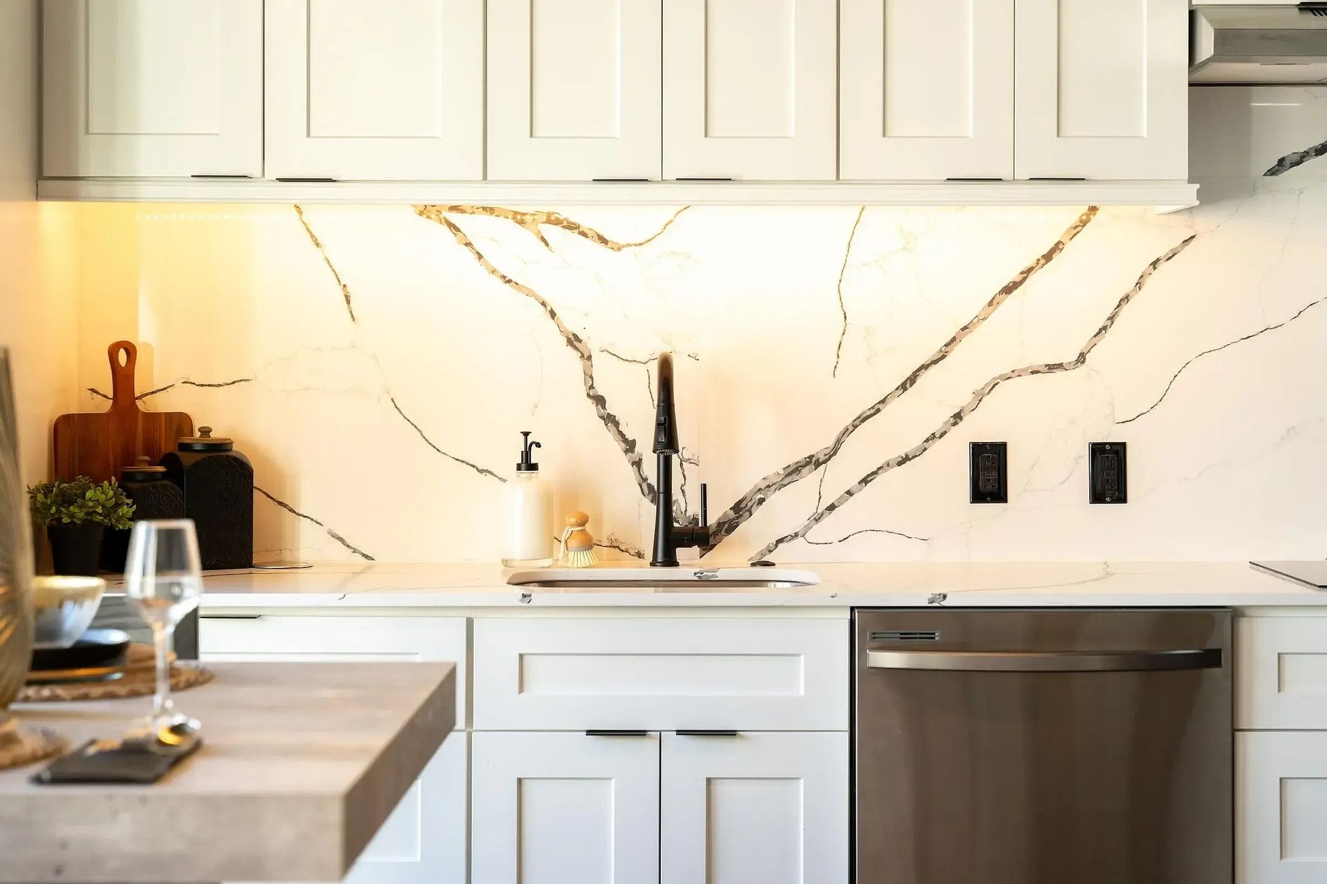 White kitchen with marble backsplash, dark faucet, and stainless steel dishwasher.