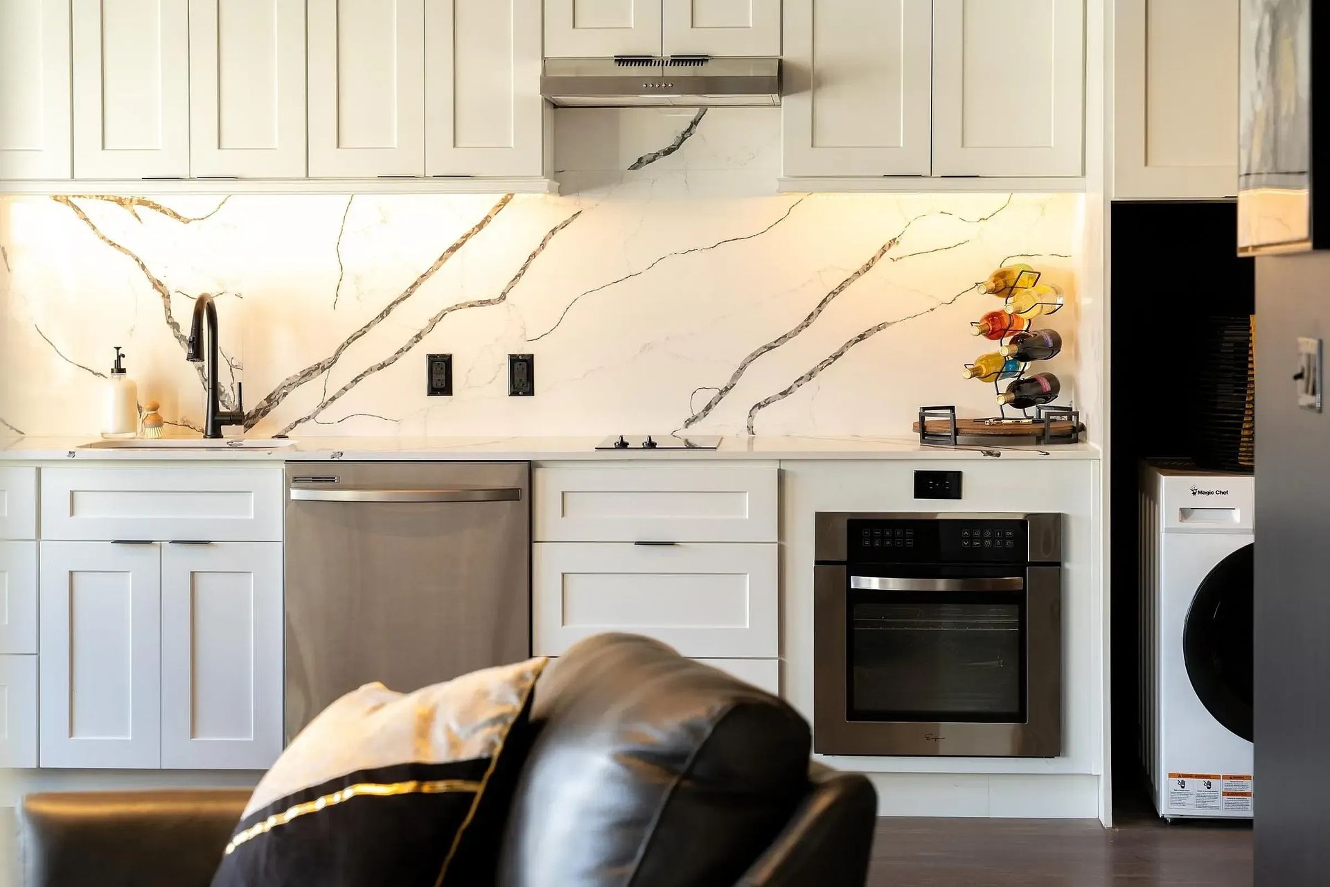 Modern kitchen with white cabinets, marble backsplash, stainless steel appliances.