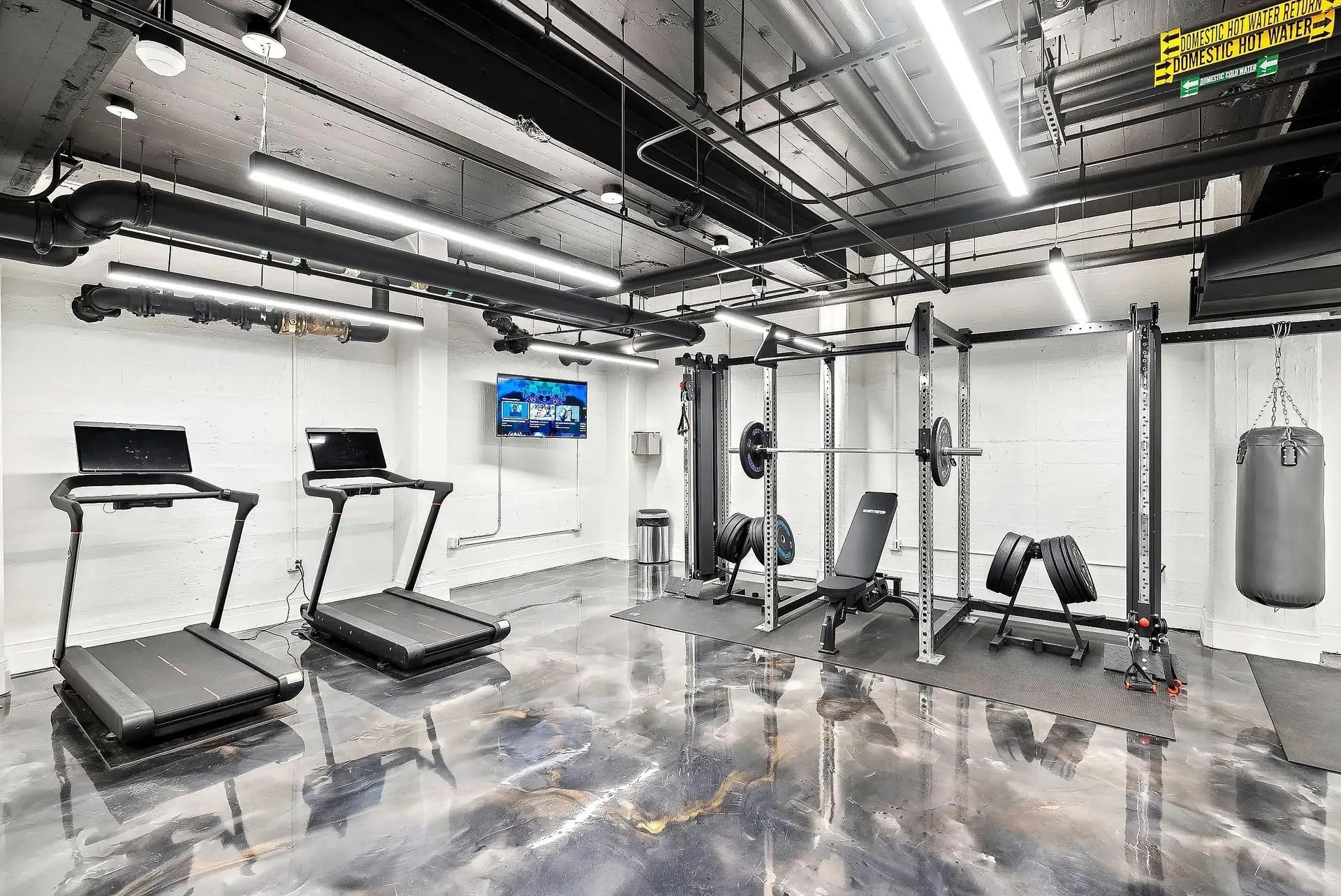 Gym interior with treadmills, weight rack, punching bag, and reflective floor.