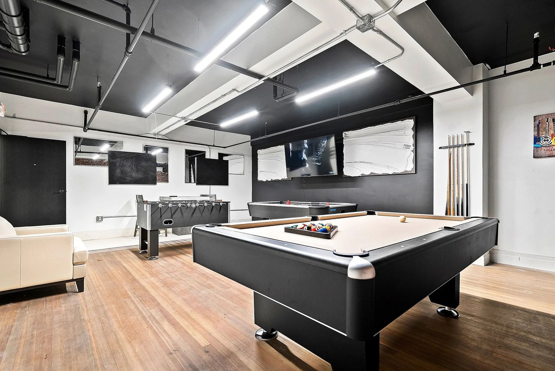 Game room with pool table, foosball, TVs, and hardwood floors.