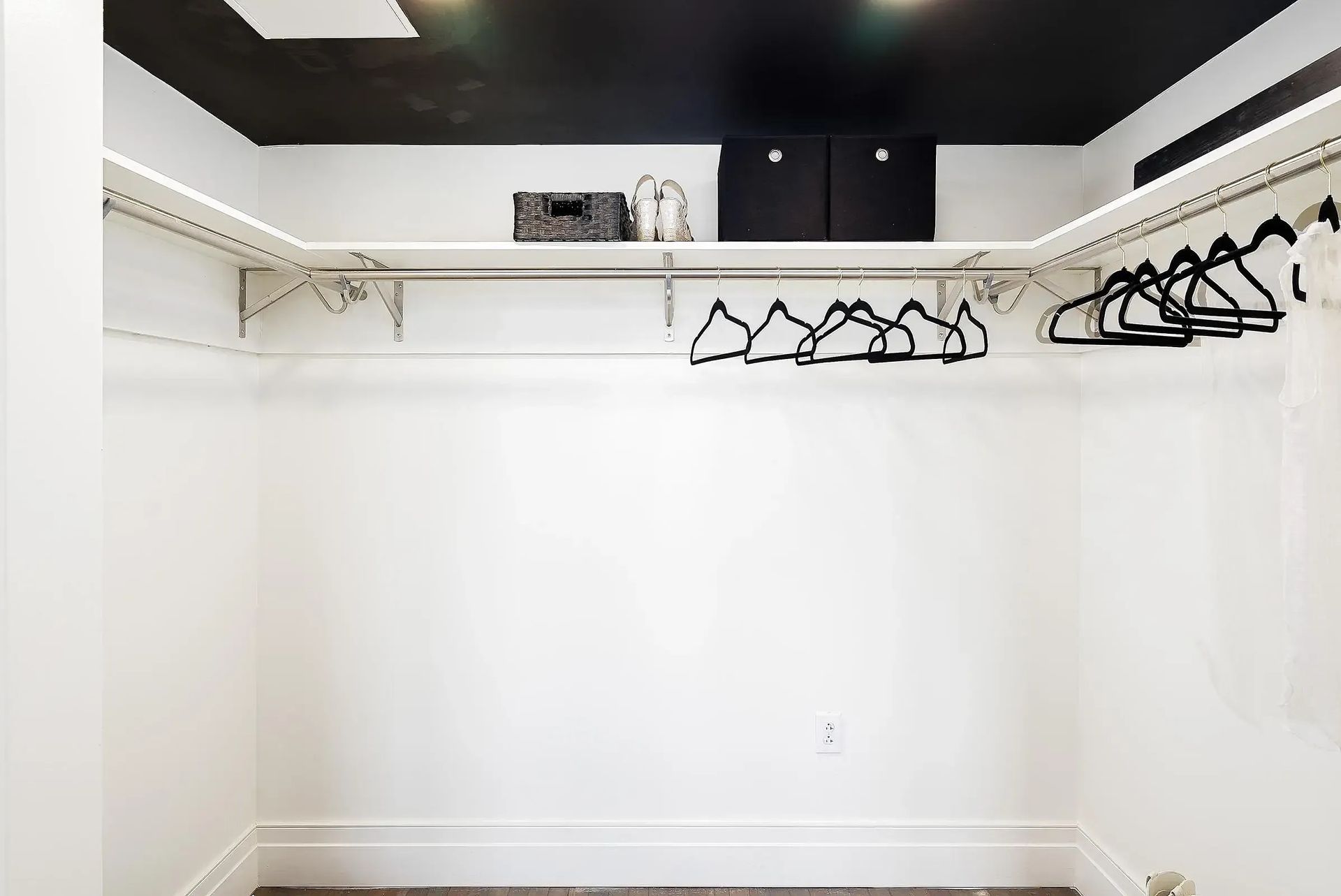 White-walled closet with black ceiling and shelves, featuring hangers and a storage box.