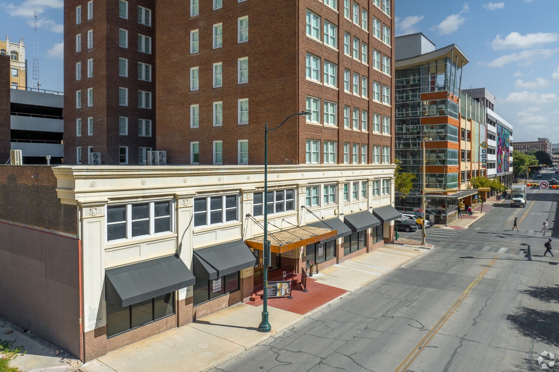 Street view of multi-story brick building with awnings, pedestrians, and modern buildings in the background.