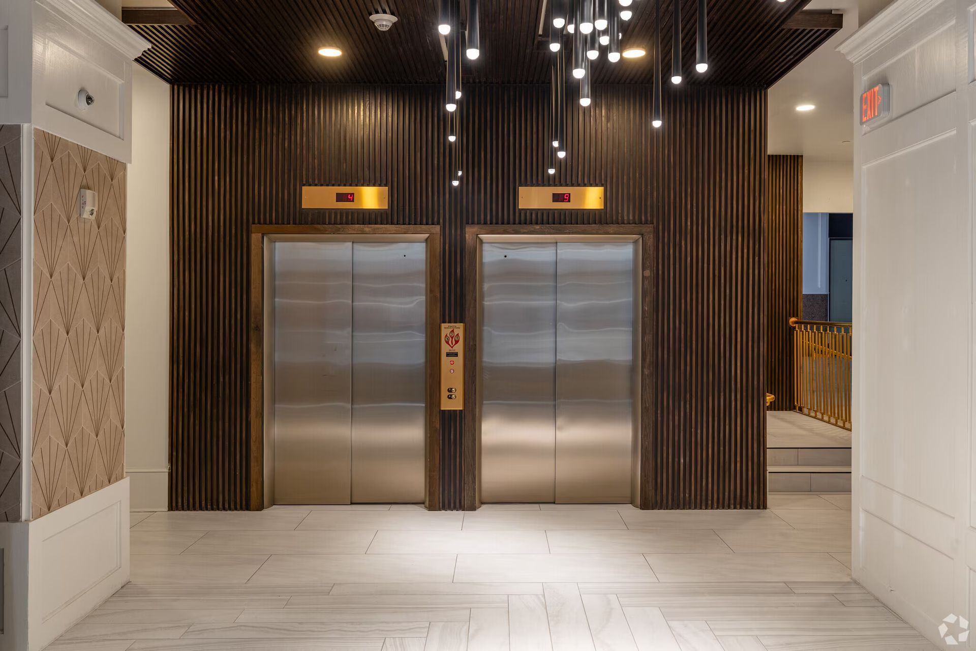Two elevator doors in a lobby with wooden paneling and modern lighting.