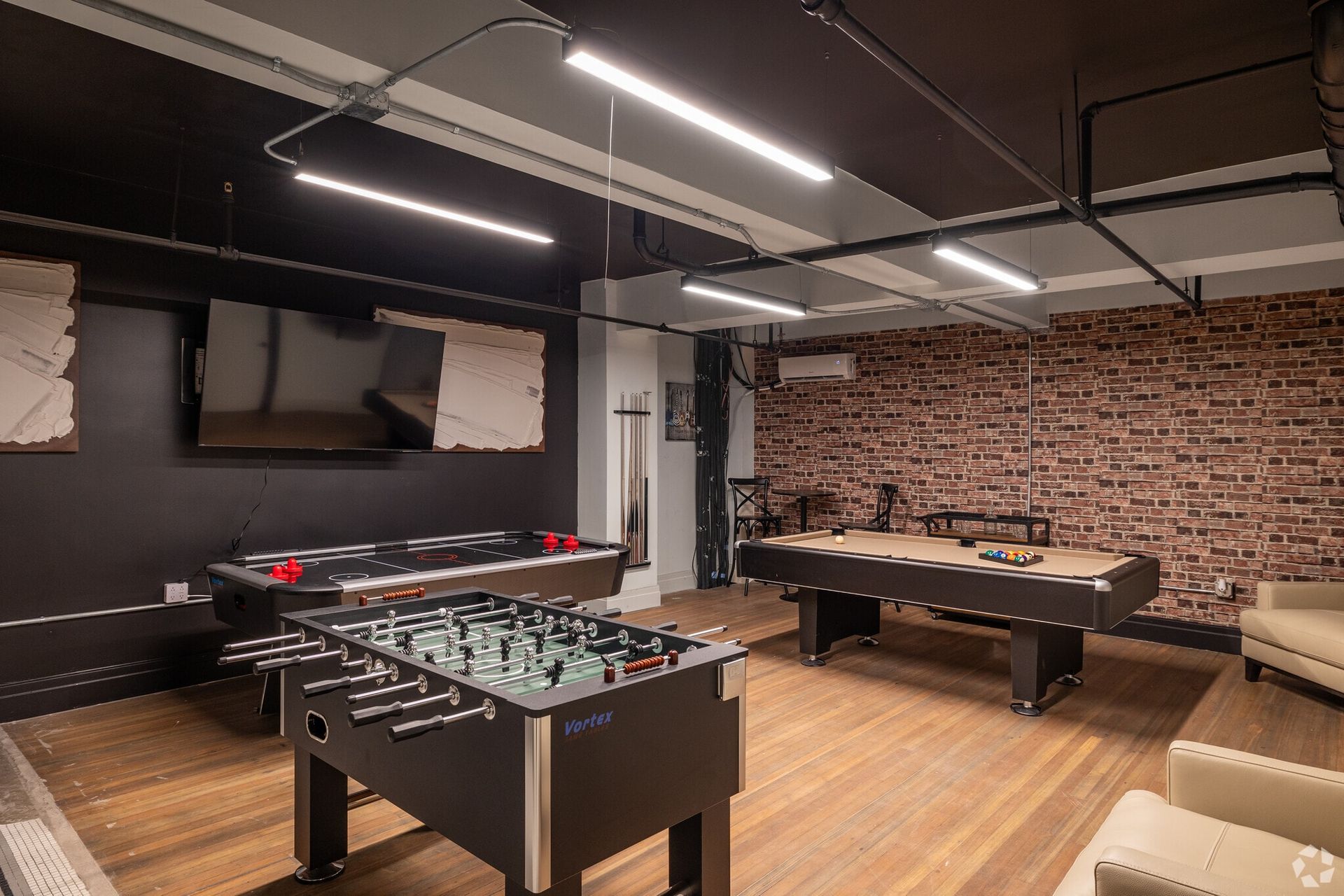 Game room with foosball, air hockey, pool table, TV, brick wall, and seating.