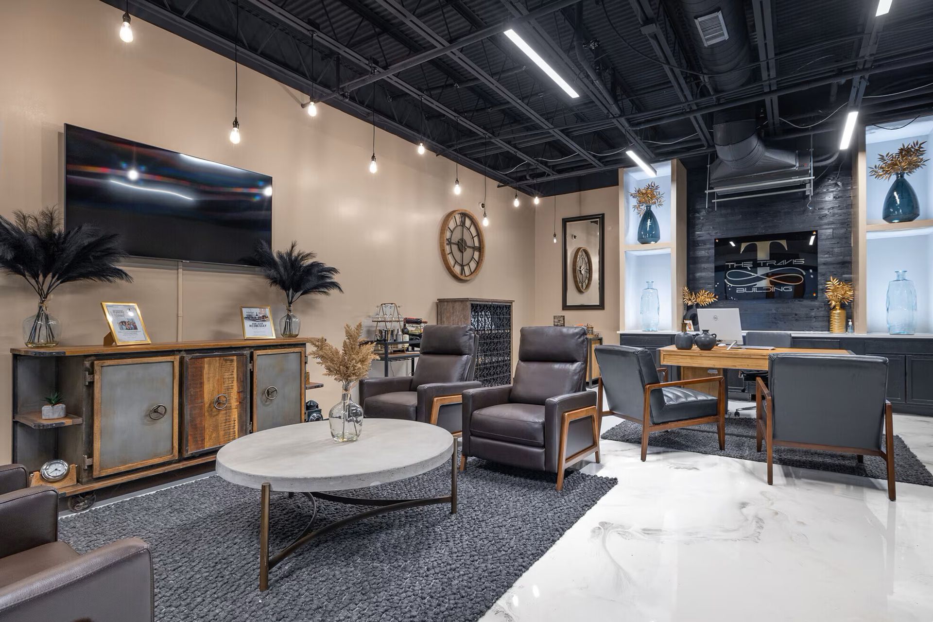 Modern showroom with furniture display: brown leather chairs, round table, TV, and black ceiling.
