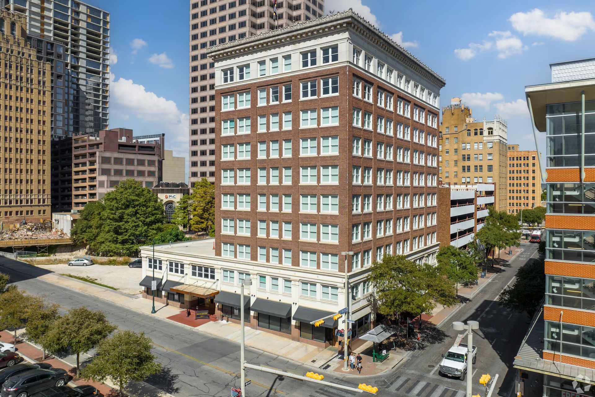 A tall brick building in a city setting with awnings over ground floor storefronts and trees.