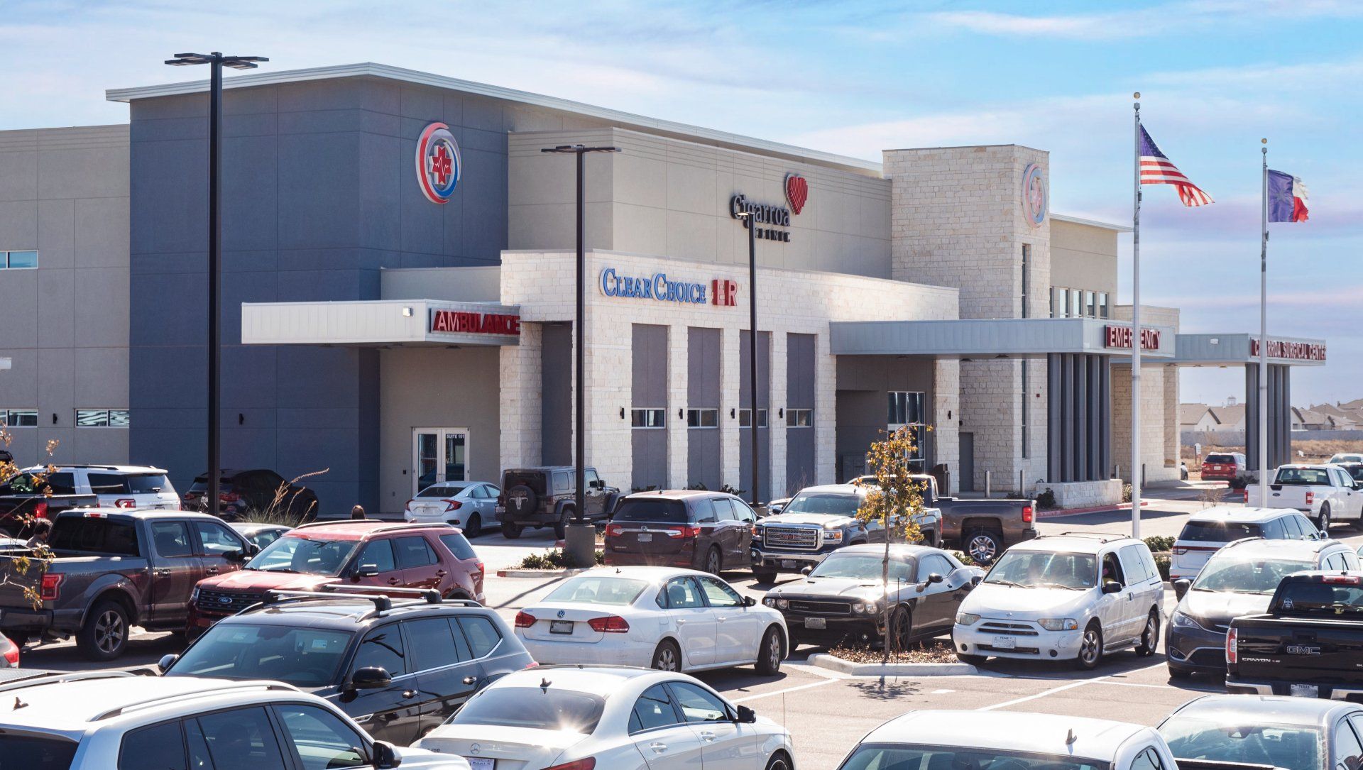 Clear Choice ER, its parking lot filled with cars. An American and Texan flag wave in front of the ER room.
