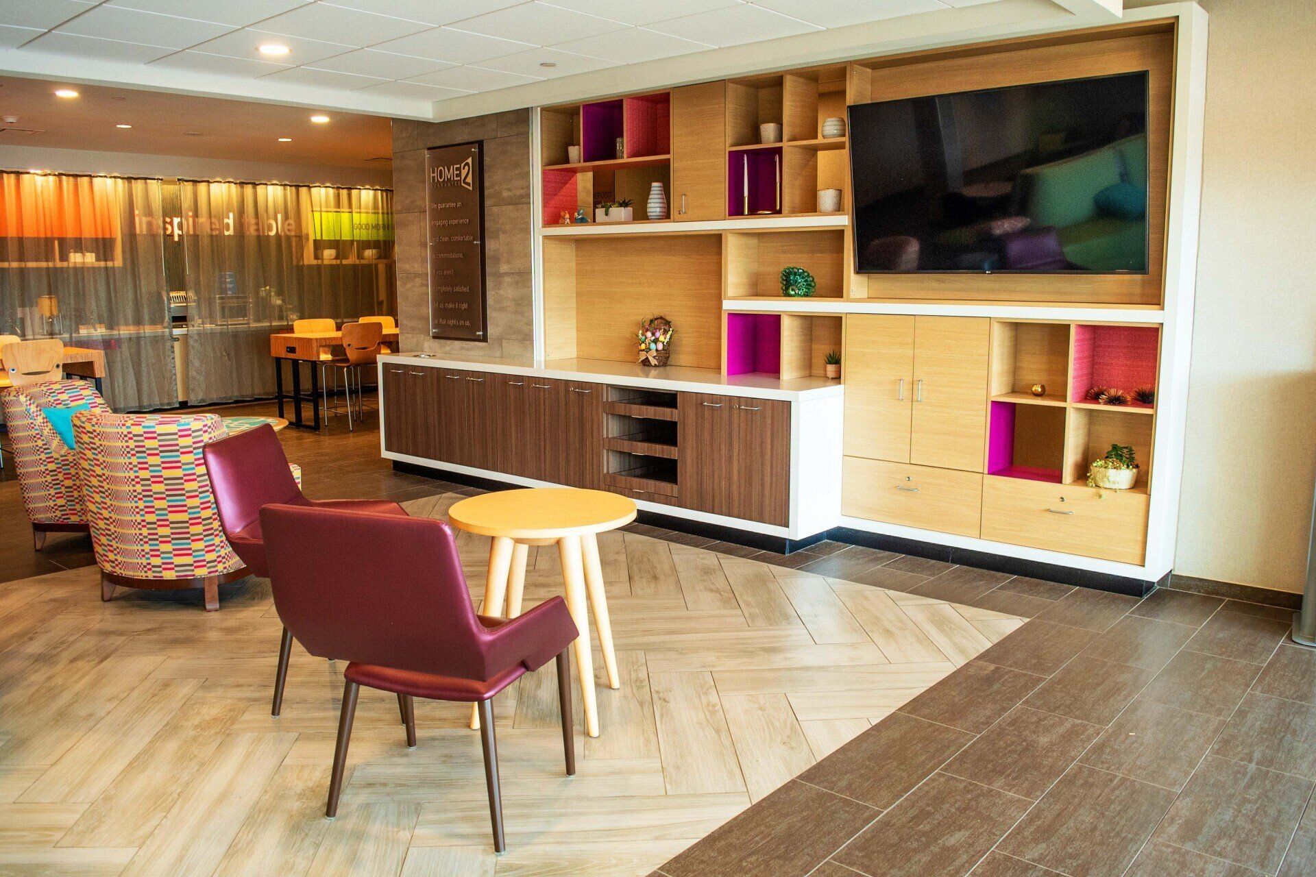 A lounge area inside the Tru Home 2 by Hilton in Laredo. Sofas and chairs are placed facing a TV mounted in the wall. 