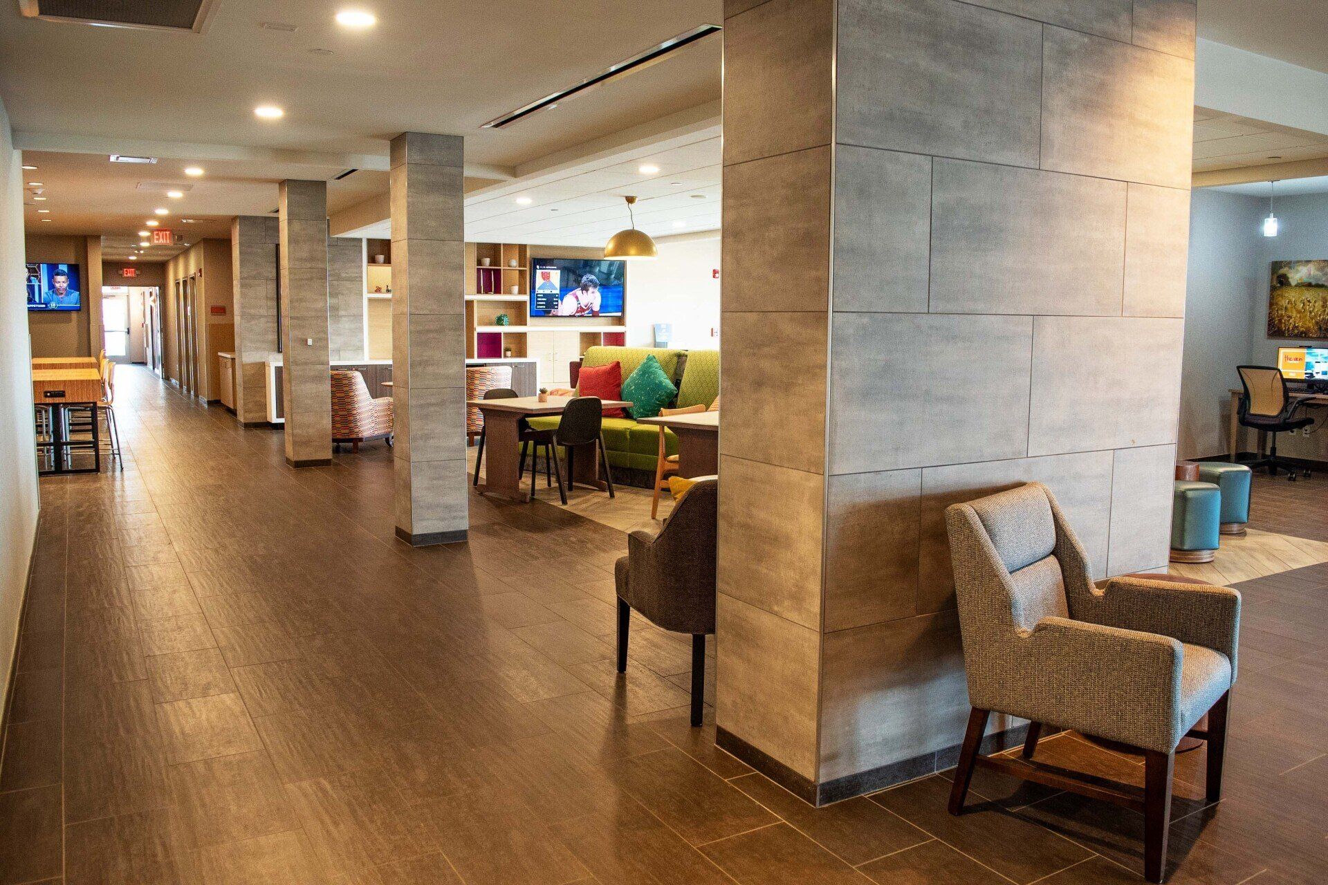 A newly built hallway inside the Tru Home 2 by Hilton. Chairs and a lounge area are featured next to the hallway. 
