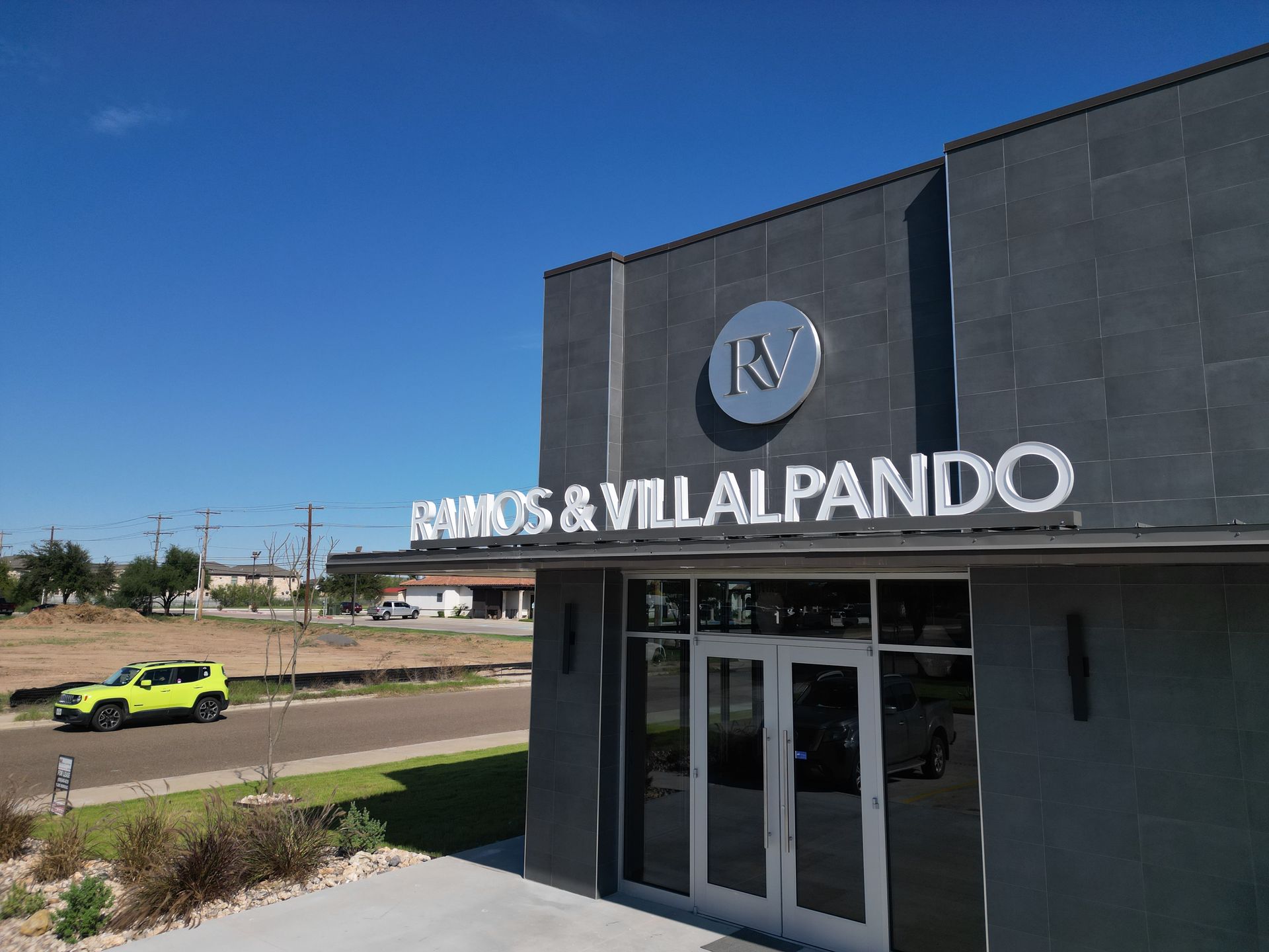 The exterior of the Ramos & Villalpando offices. A bright green car is visible on the road next to it.
