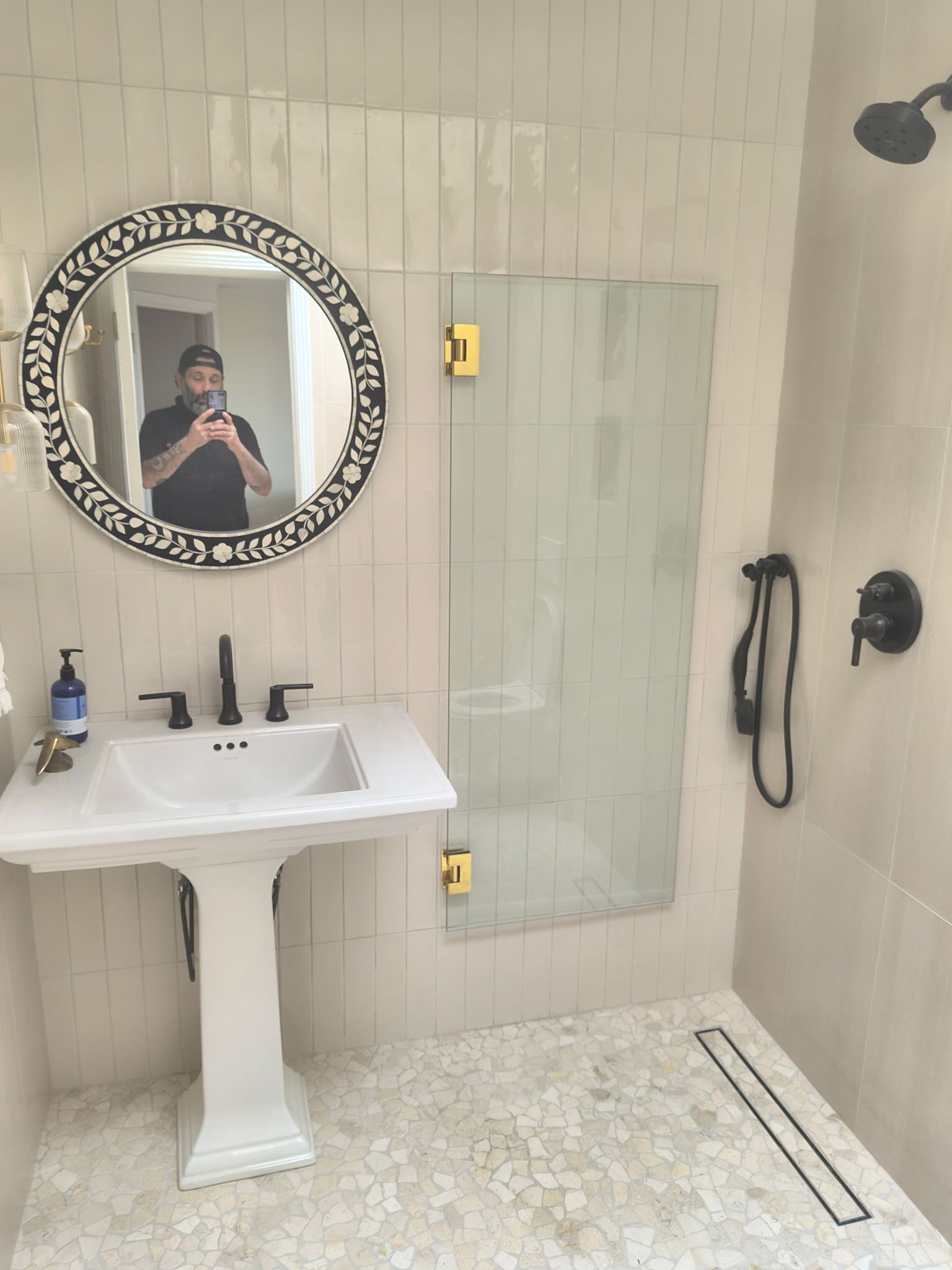 A man taking a photo of a bathroom with a sink, mirror and shower.