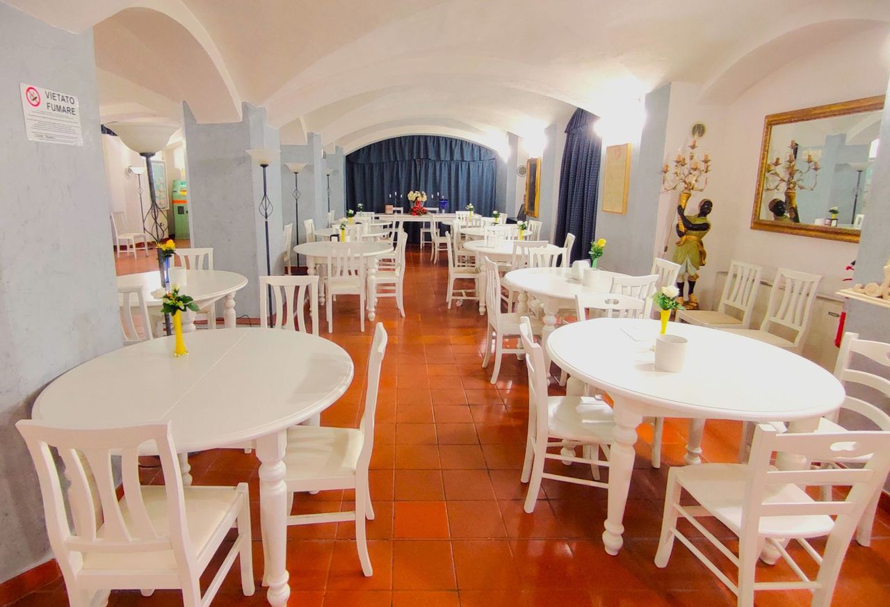 Bright dining room with white tables and chairs, red tile floor, and a blue curtained stage at the back