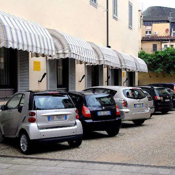 Row of parked cars beside a cream building with striped awnings in a quiet courtyard