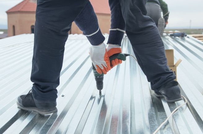 Man installing metal sheet roof by electrical drilling machine