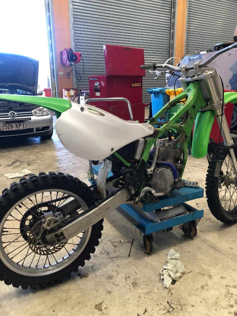 Green and white dirt bike in a garage setting, undergoing repairs. — Bodes All Mechanical In Bega, NSW