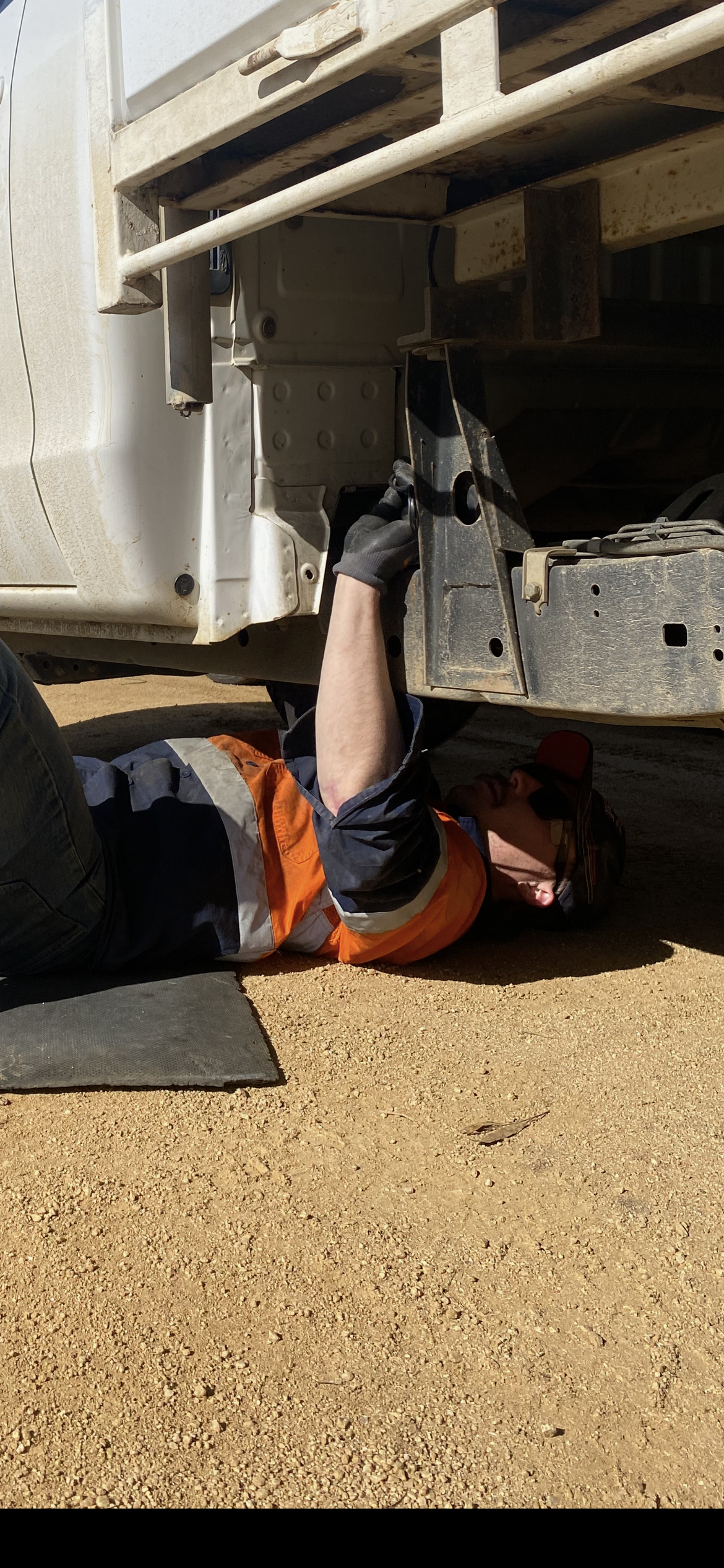 A person wearing an orange vest works under a vehicle on gravel. — Bodes All Mechanical In Bermagui, NSW