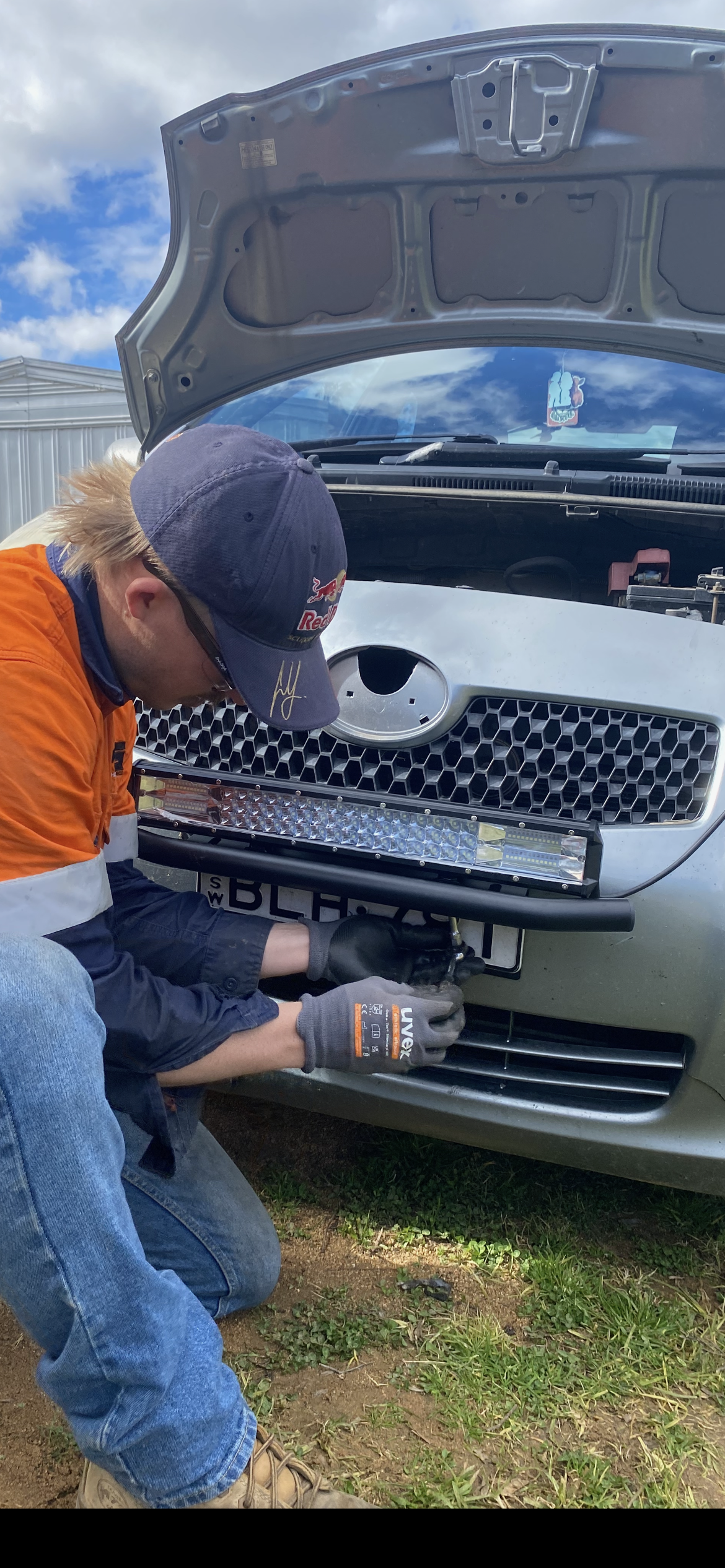 A Person Installs a Light Bar on the Front of a Silver Car, Outdoors — Bodes All Mechanical In Bermagui, NSW