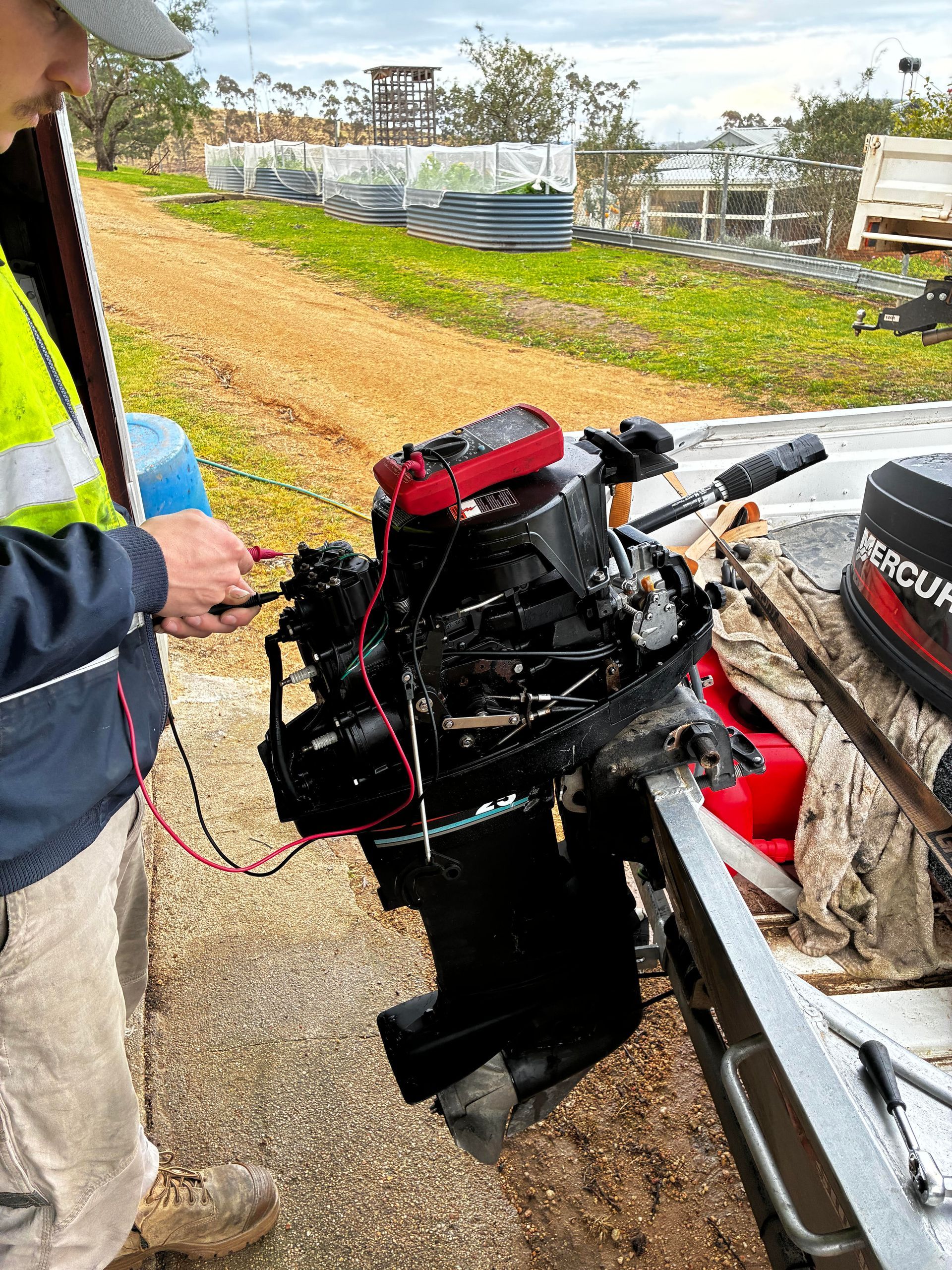 Man repairs boat motor with multimeter outside. Black motor, Mercury logo. — Bodes All Mechanical In Bombala, NSW
