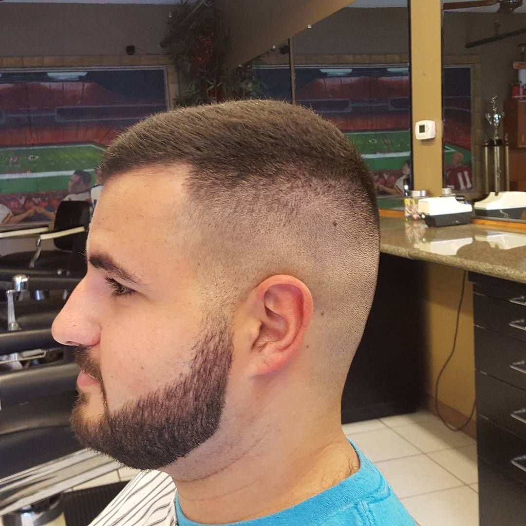 A man with a beard is getting his hair cut by a barber