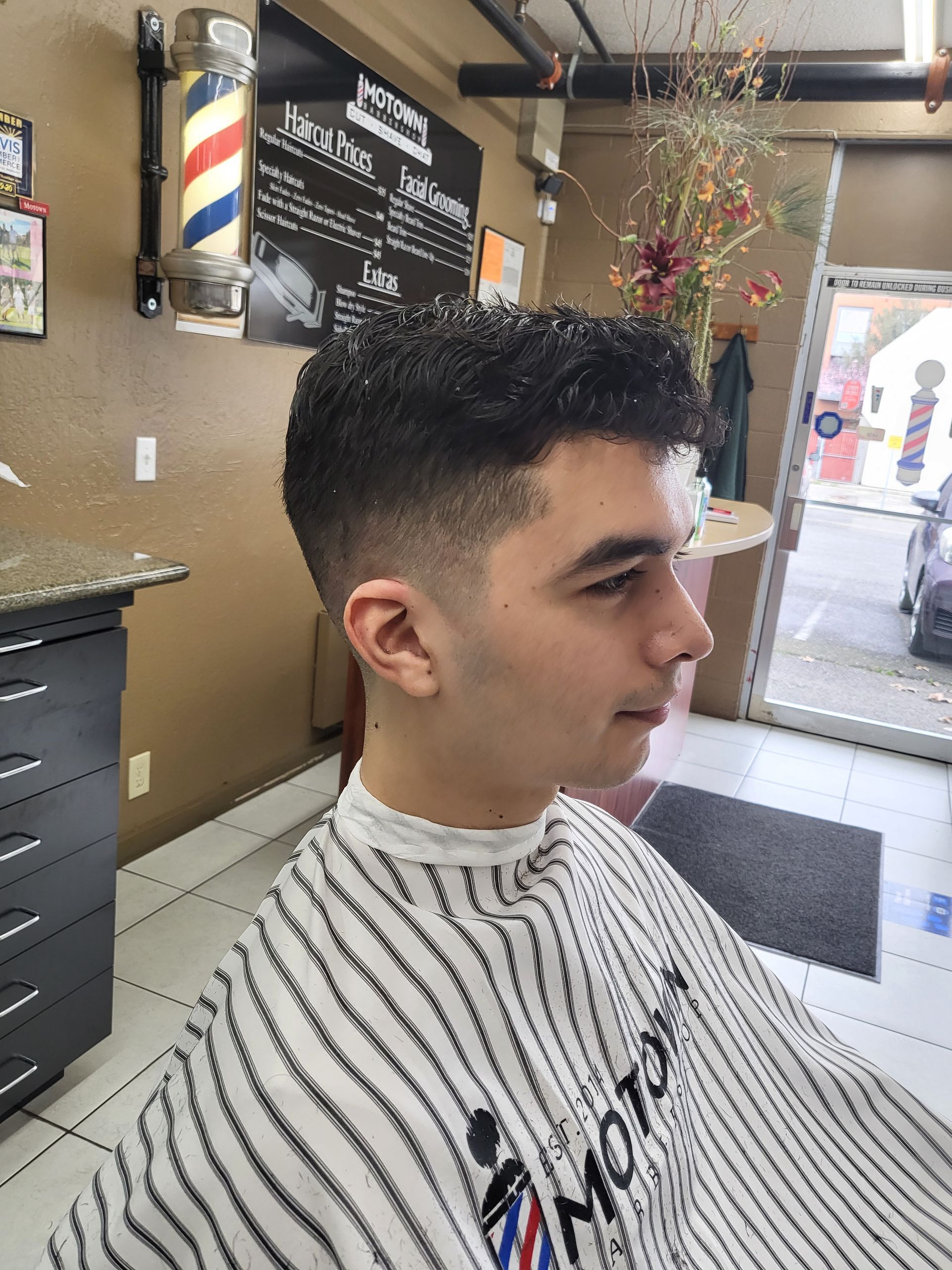A young man is getting his hair cut at a barber shop.
