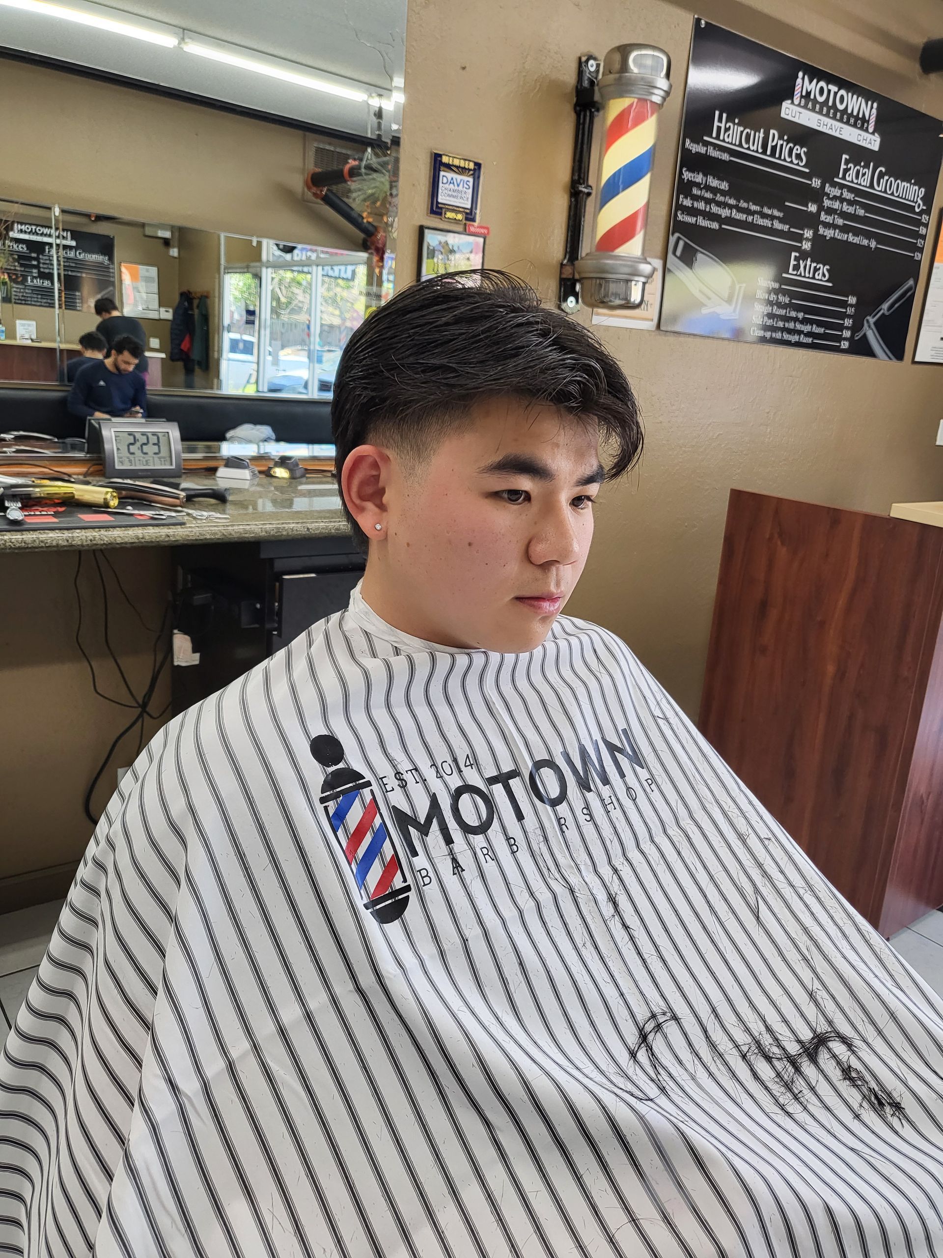 A young man is getting his hair cut at a barber shop.
