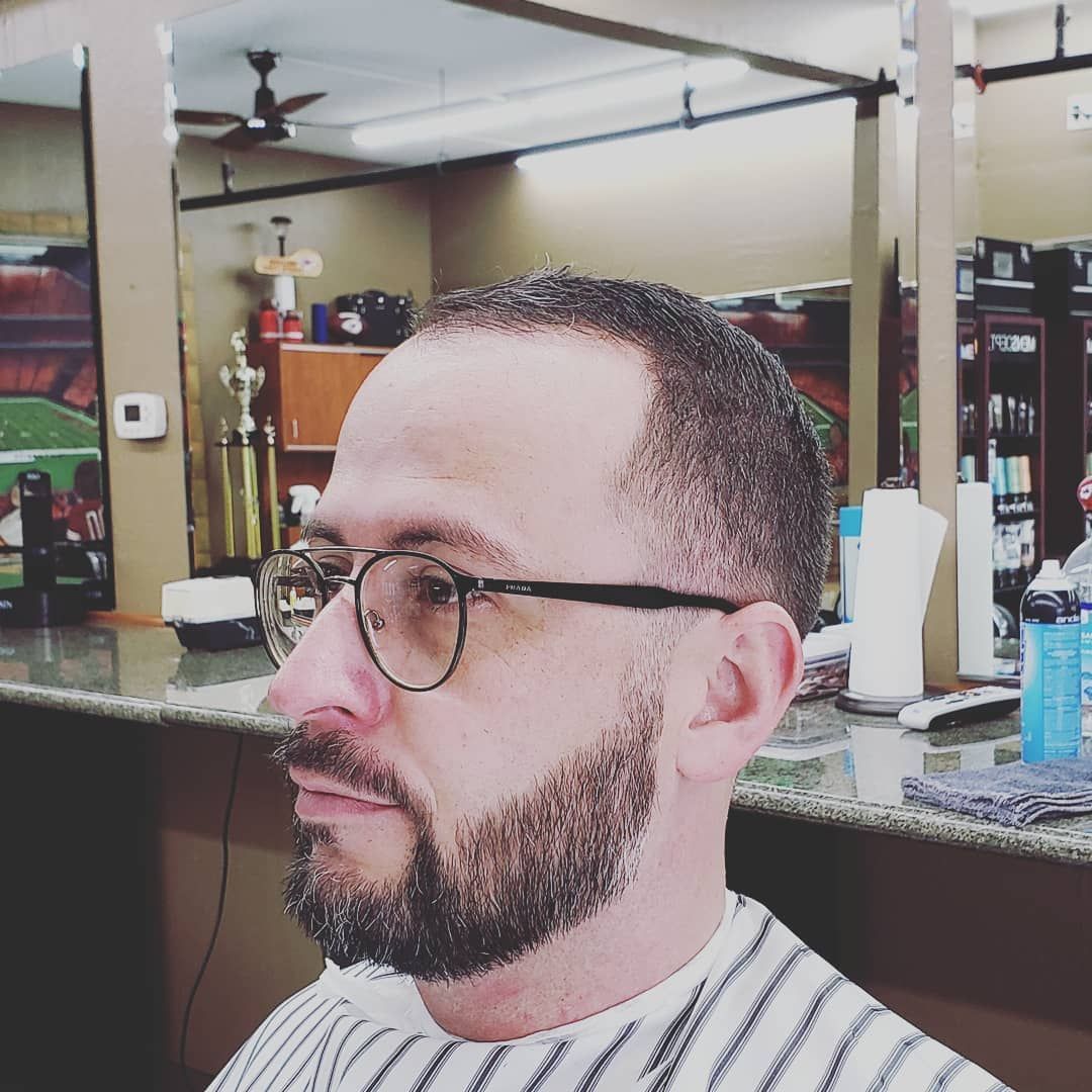 A man with glasses and a beard is getting his hair cut at a barber shop