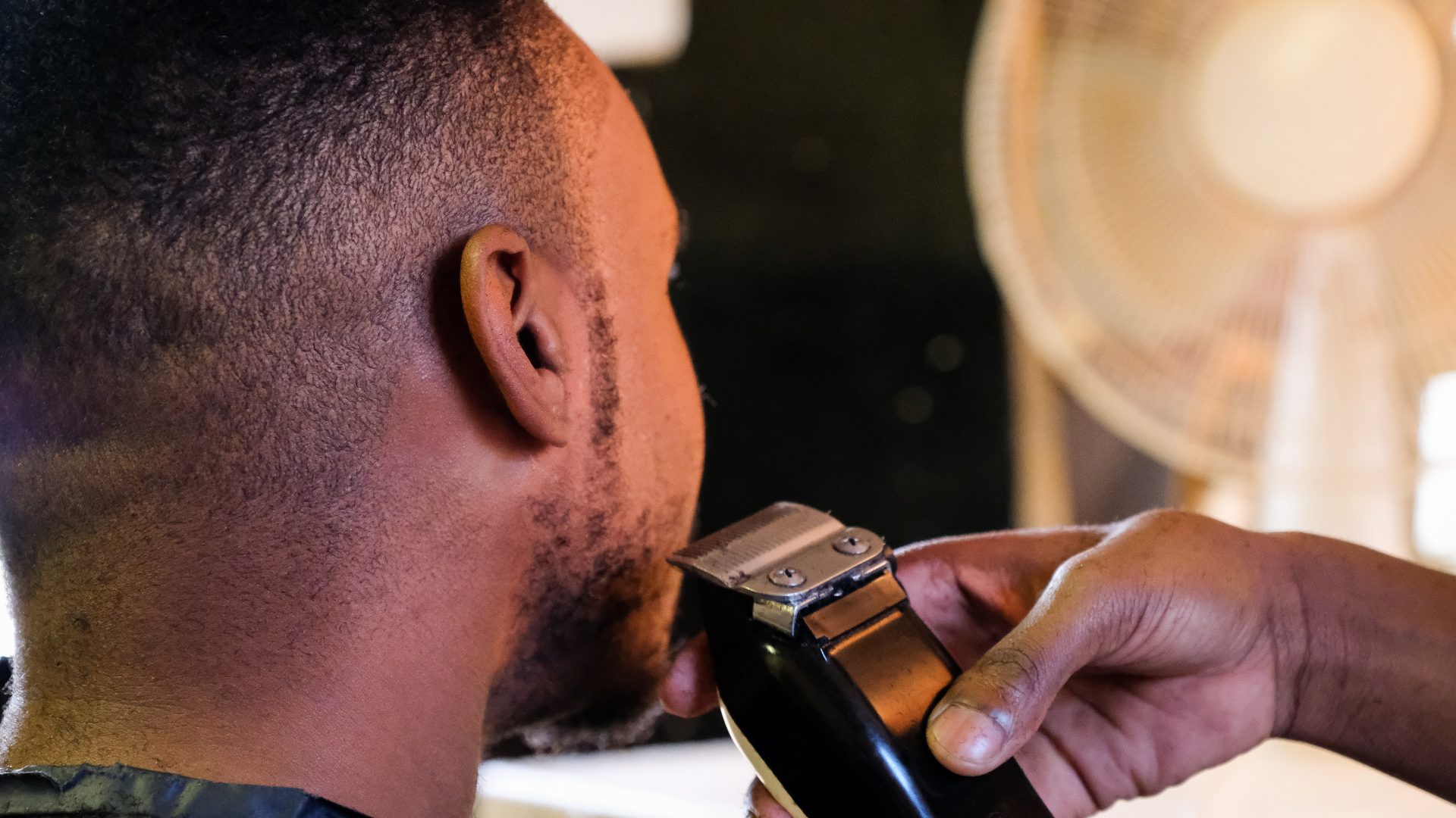 A man is getting his hair cut by a barber with a clipper.
