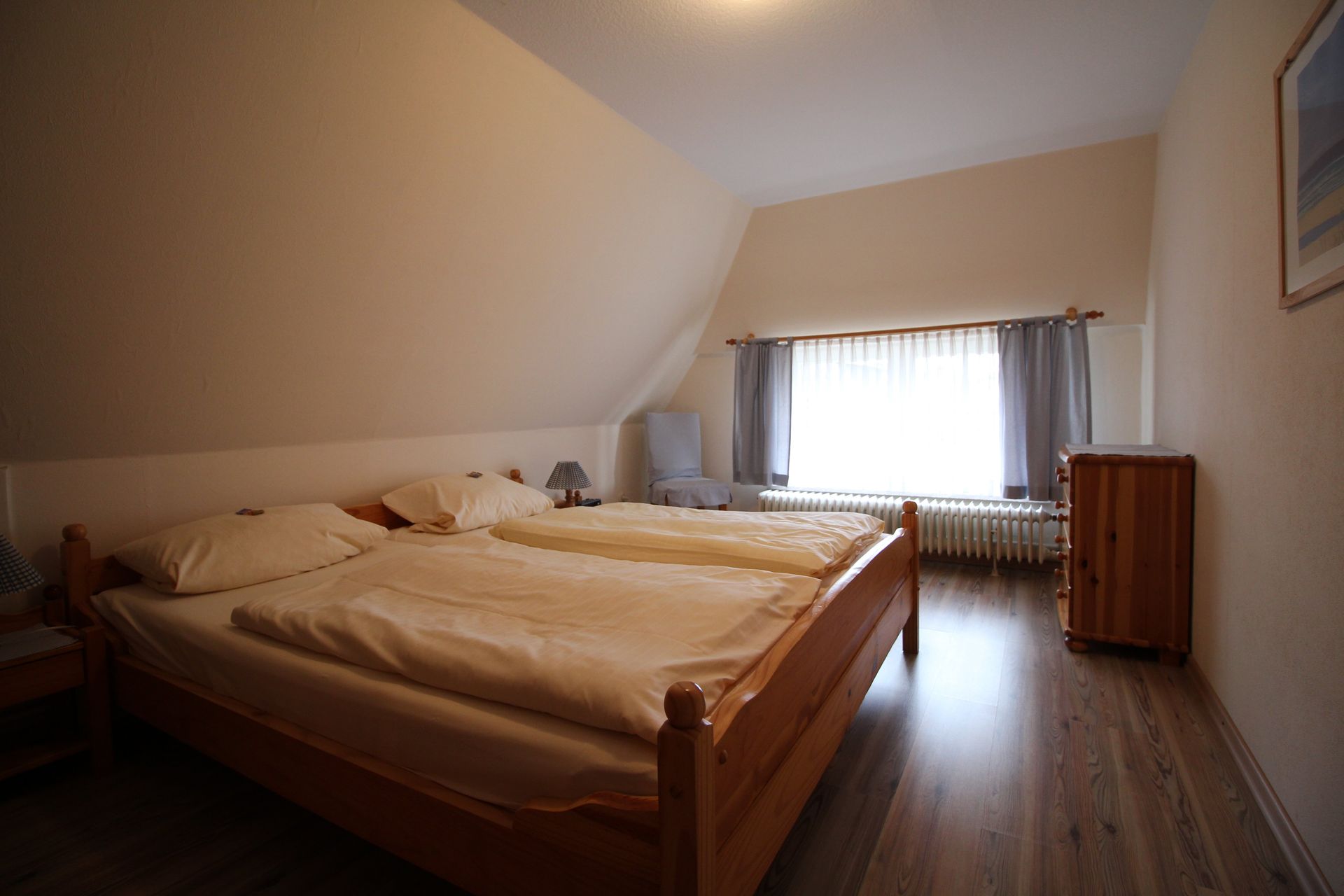 Bedroom with a wooden bed, wooden floor, and a large window with curtains.