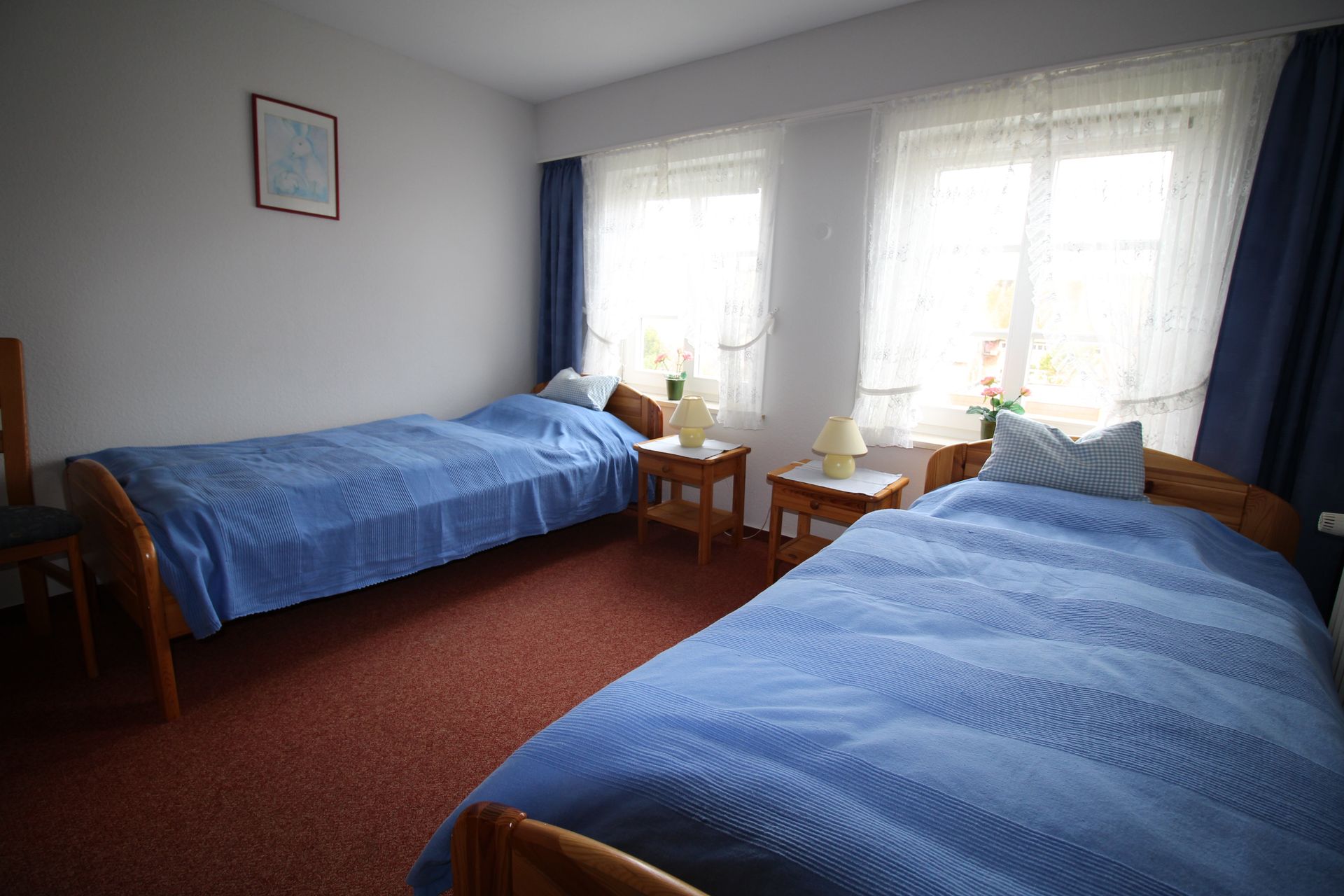 Two twin beds with blue bedding, nightstands, and windows with blue curtains.