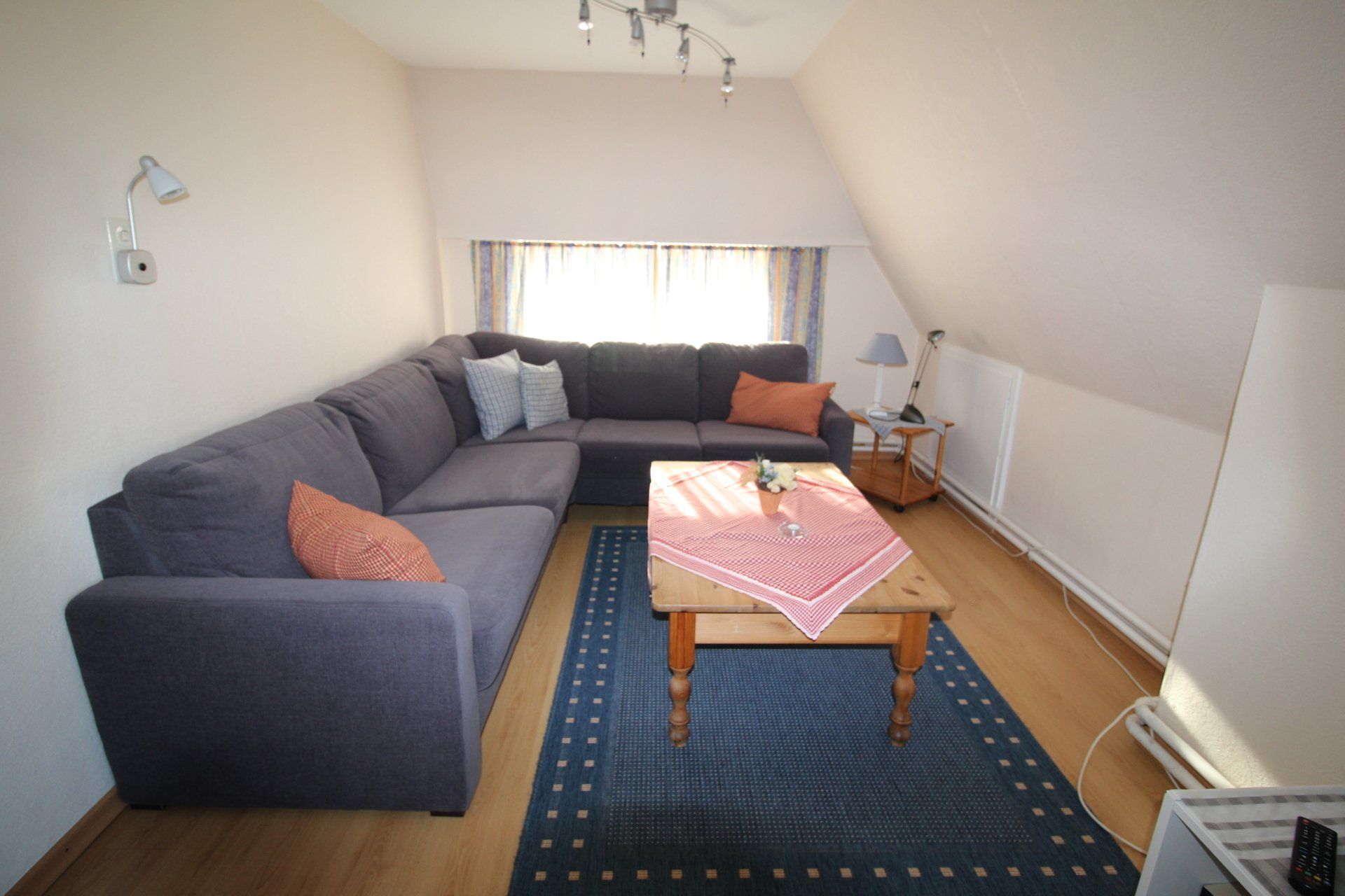 Cozy attic living room with a blue sectional sofa, wooden coffee table, and a blue rug. 