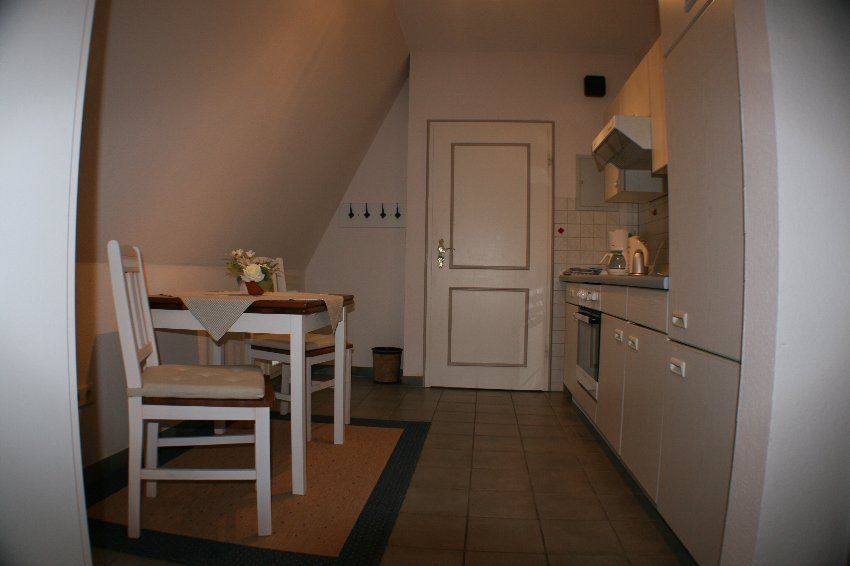 Small kitchen with a white door, cabinets, and a table with chairs. The room has an angled ceiling and tile floor.
