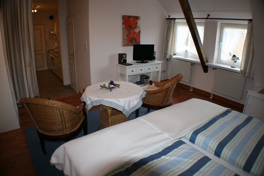 Bedroom with a bed, two wicker chairs, a table, and a small TV. A doorway leads to a hallway.