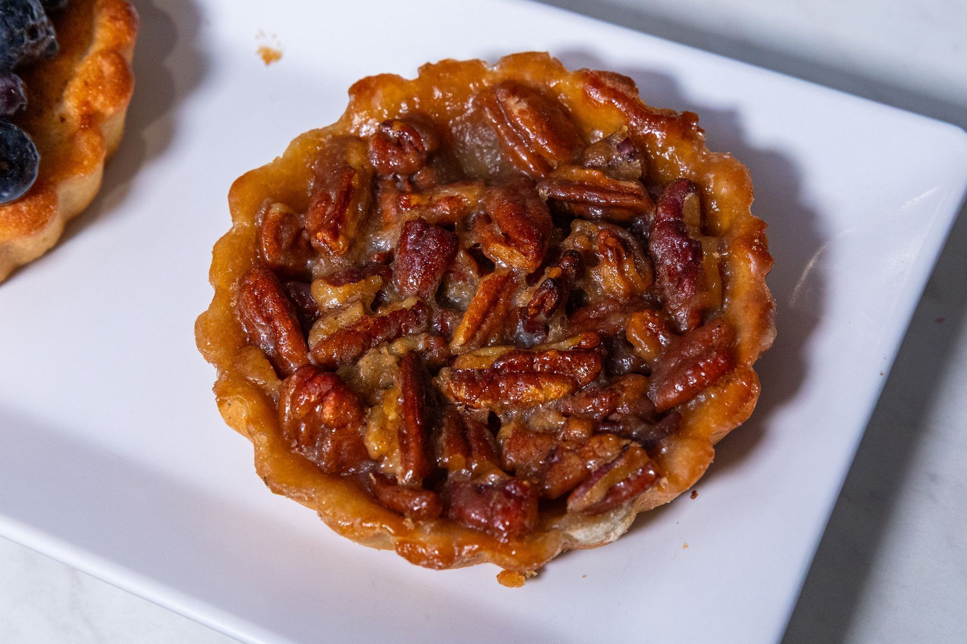 Pecan tart on a white plate, close-up with a caramelized glaze and crispy crust.