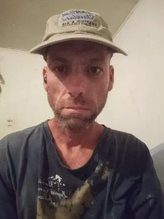 Man in a hat and dark shirt, looking directly at the camera with a serious expression.