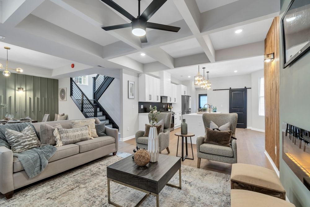 Living room with open layout: couch, chairs, coffee table, kitchen in the background.