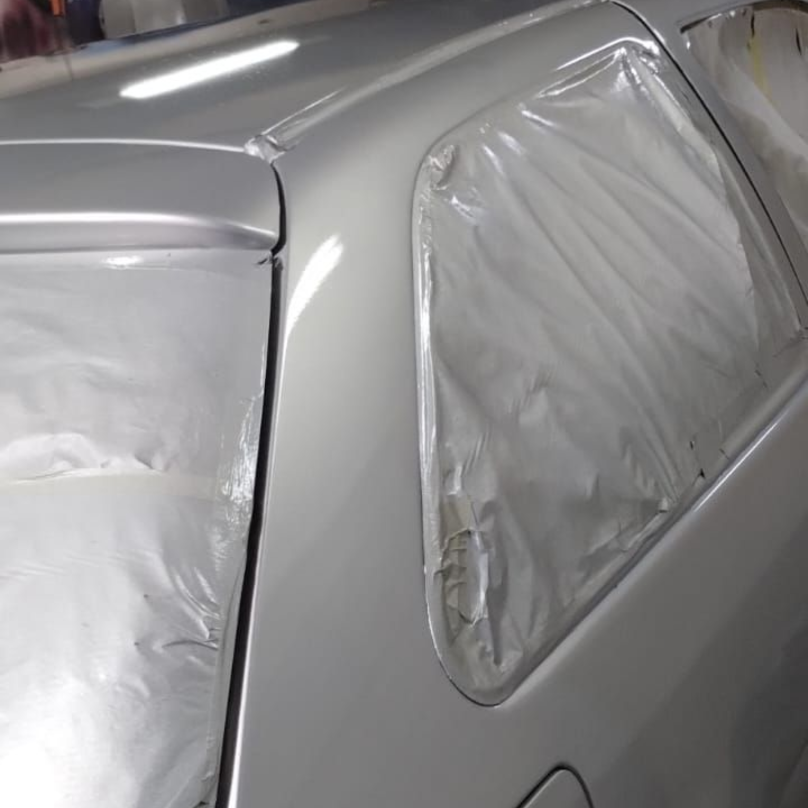 Panel trasero de un coche plateado, con las ventanas cubiertas con plástico, recién pintado, en un taller.