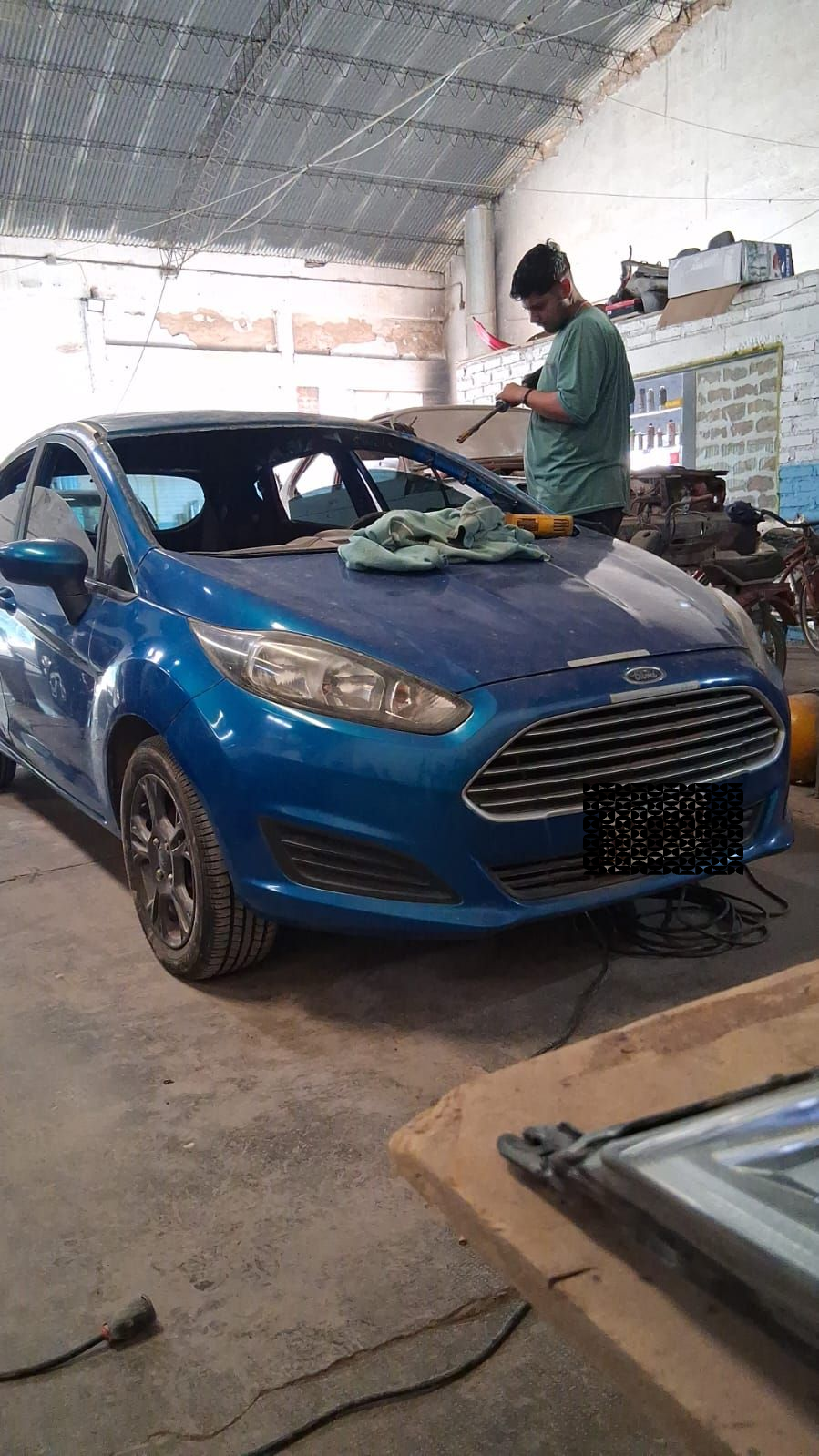 Coche Ford azul en un garaje con una persona trabajando en el parabrisas.